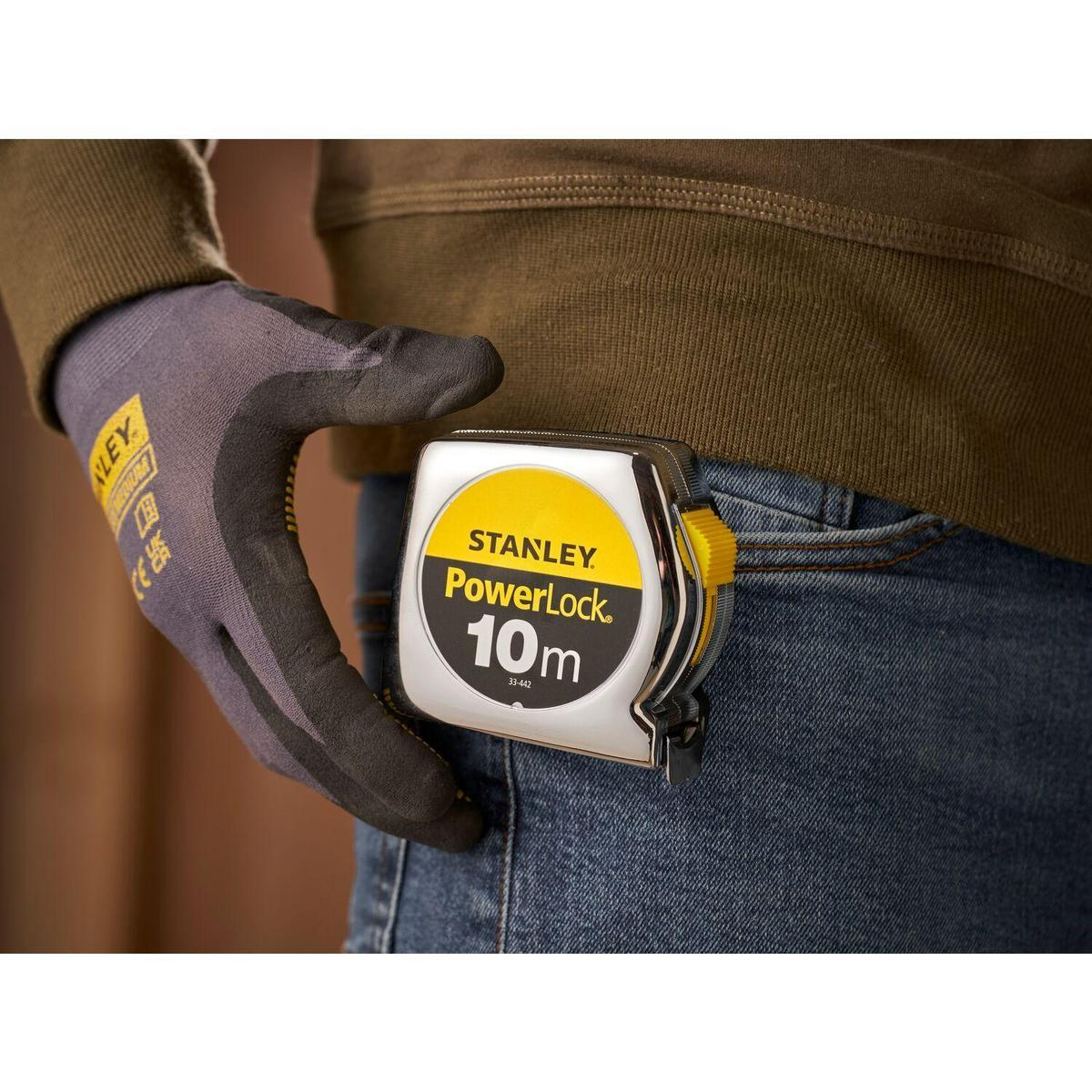 Die Hand einer Person mit Handschuh hält ein Stanley PowerLock 10m Maßband auf Jeans.
