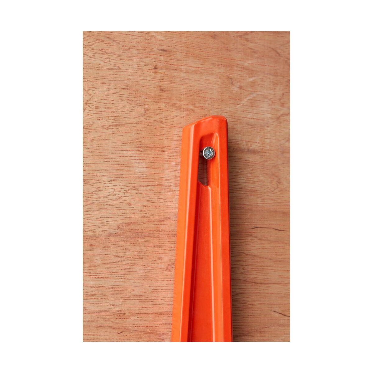 Una herramienta de nivel naranja, con un tornillo en el centro, sobre una textura de madera.