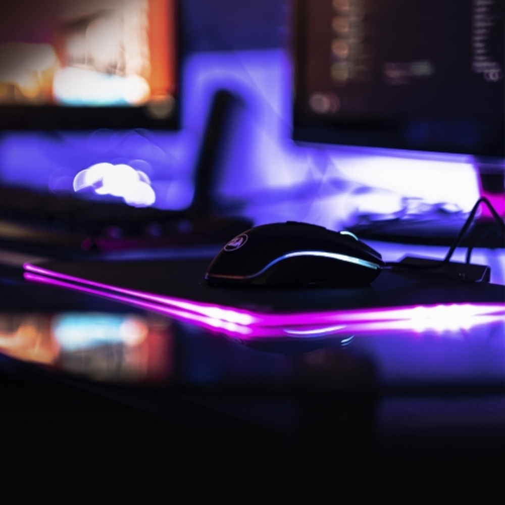 Konfiguracja do gier z czarną myszą i klawiaturą. Fioletowe i różowe oświetlenie, ciemne otoczenie.