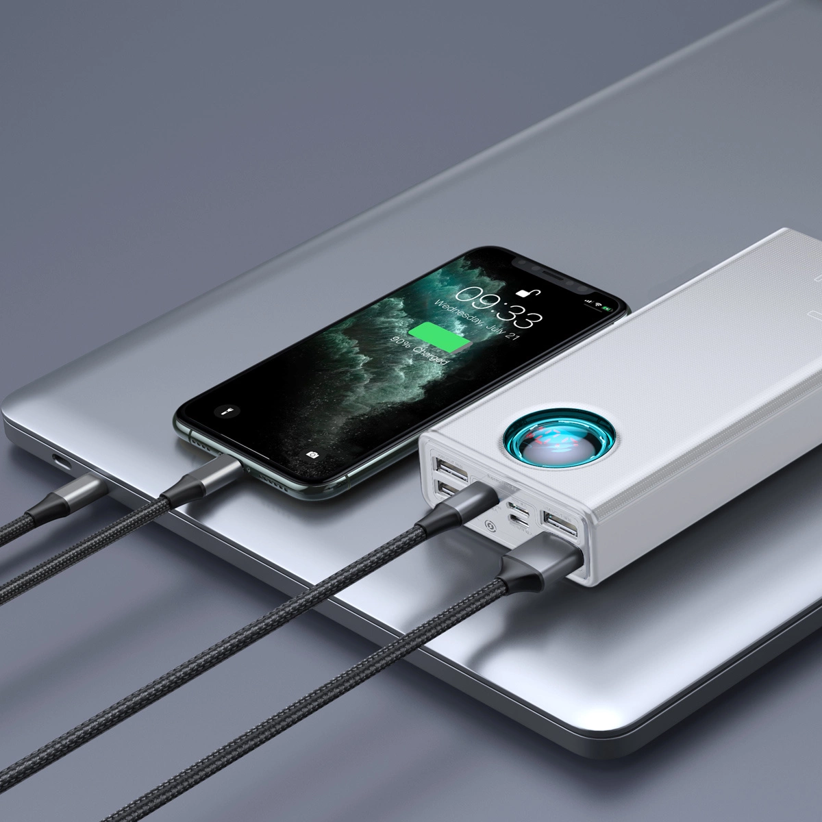 Telefon ładujący się na srebrnej powierzchni, podłączony do białego power banku czarnymi kablami.