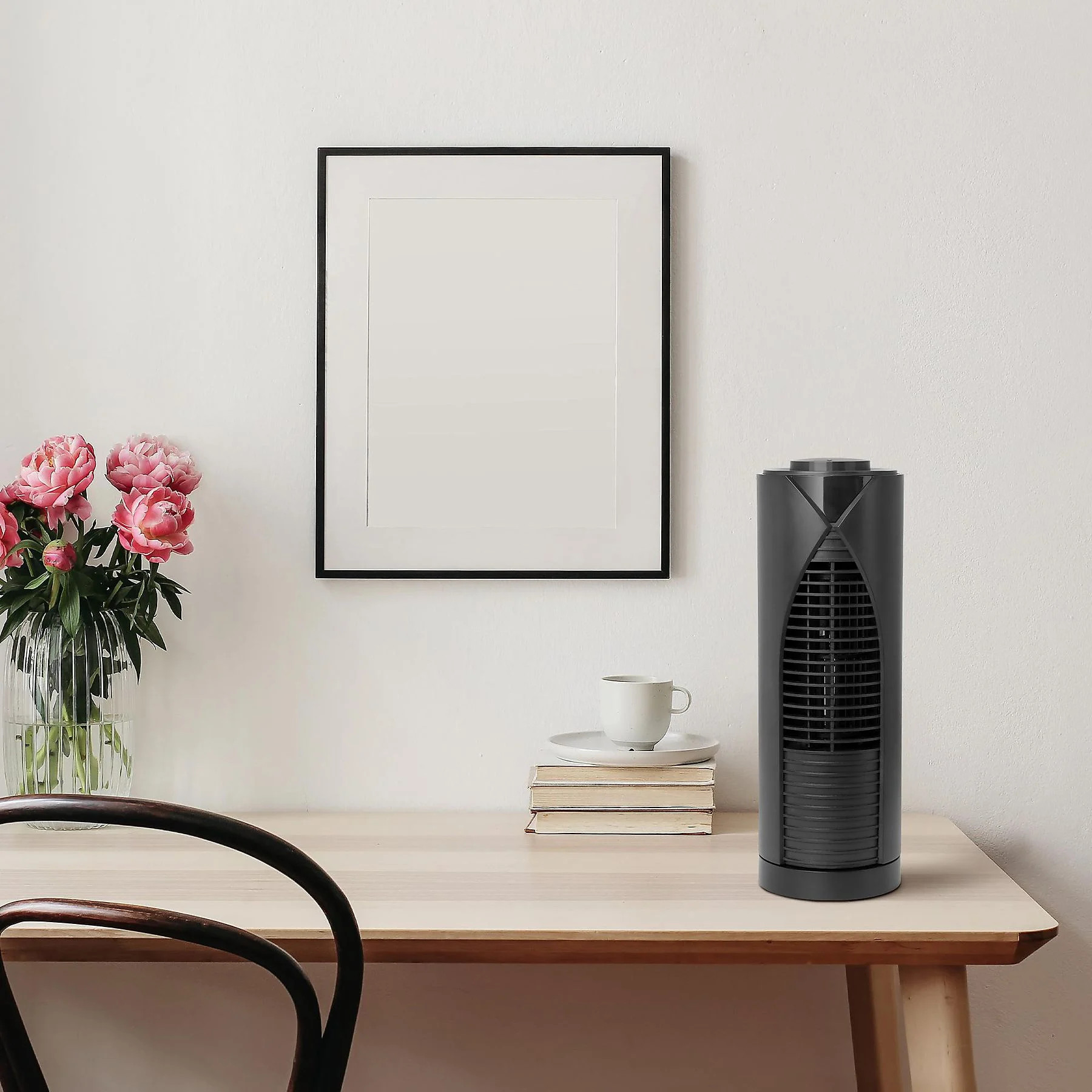 Ein schwarzer Turmventilator auf einem Schreibtisch mit gerahmtem Bild, Blumen in einer Vase und einer Tasse. Innenansicht.