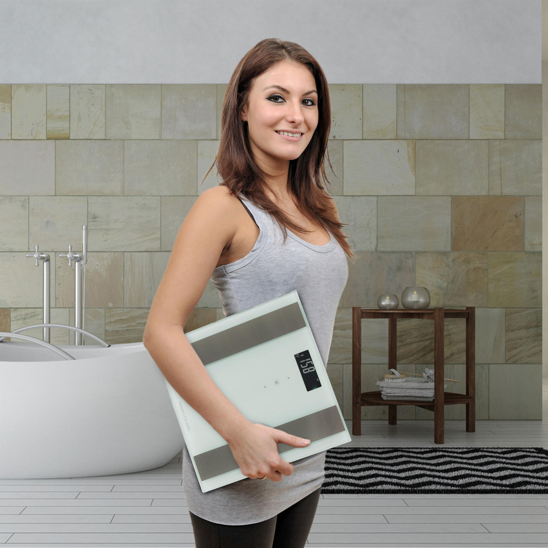 Kobieta trzymająca wagę w łazience. Pokazuje 58 kg.