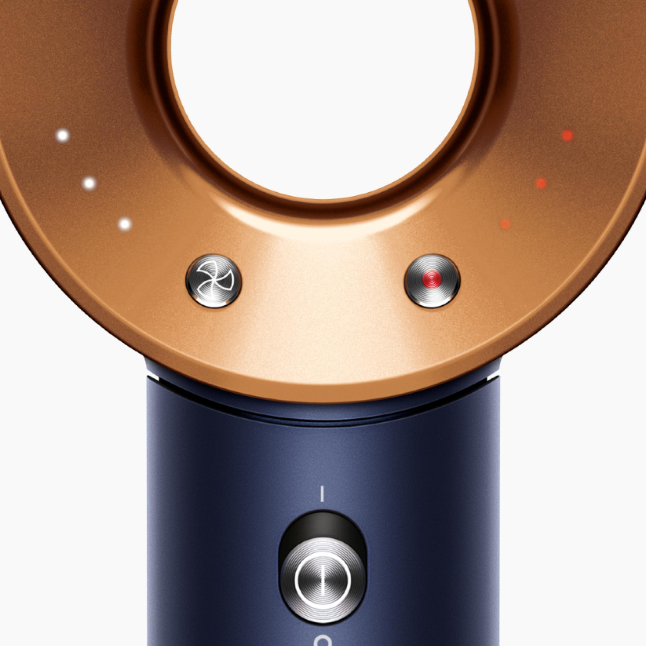 Zbliżenie suszarki do włosów pokazuje okrągłą, złotą głowicę z białymi i czerwonymi światłami oraz niebieskim uchwytem.