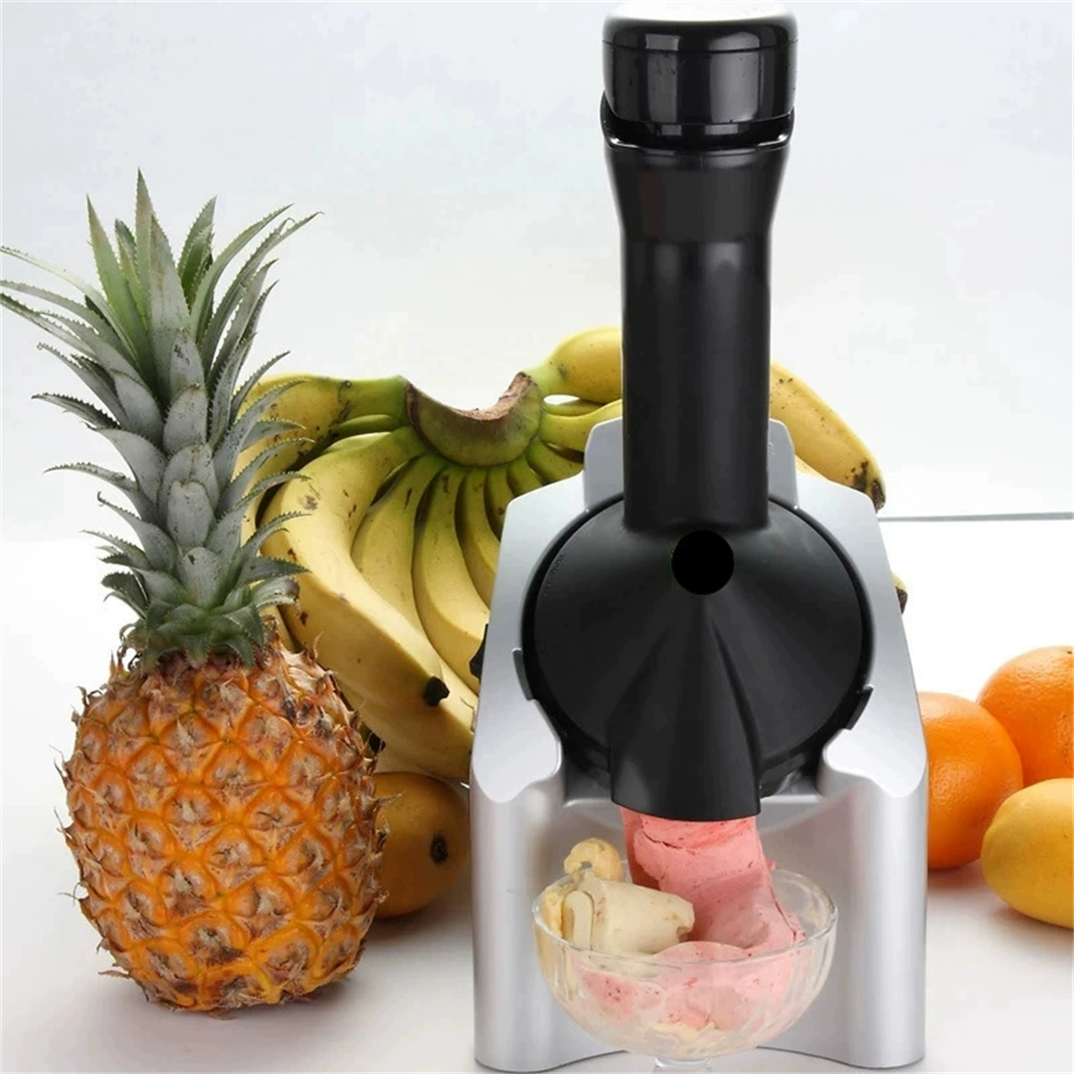 Eine Eismaschine mit Ananas und Bananen. Rosa Eis in einer Schüssel. Andere Früchte in der Szene.