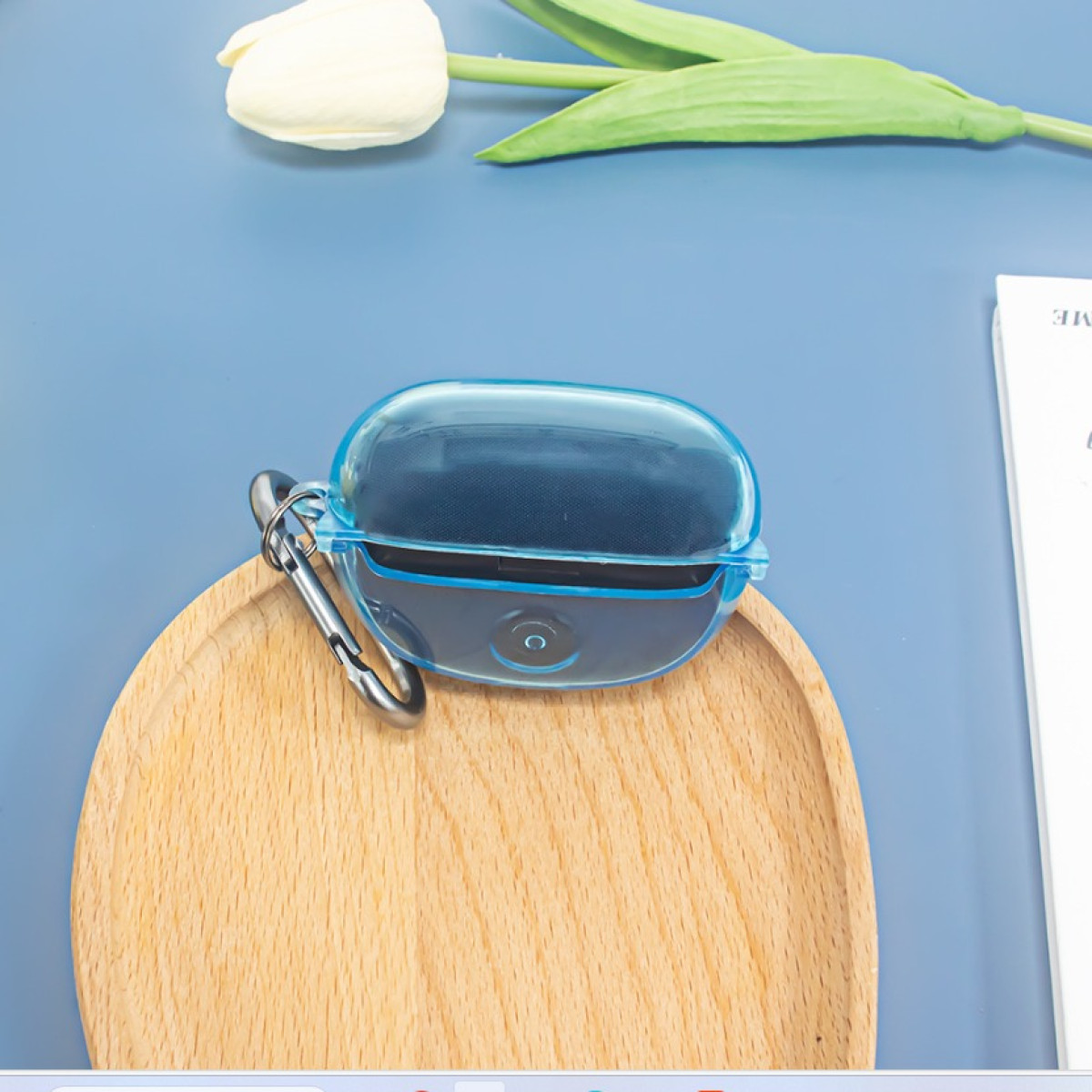 Eine blaue Ohrhörerhülle mit einem silbernen Clip auf einem Holztablett auf einer blauen Oberfläche.