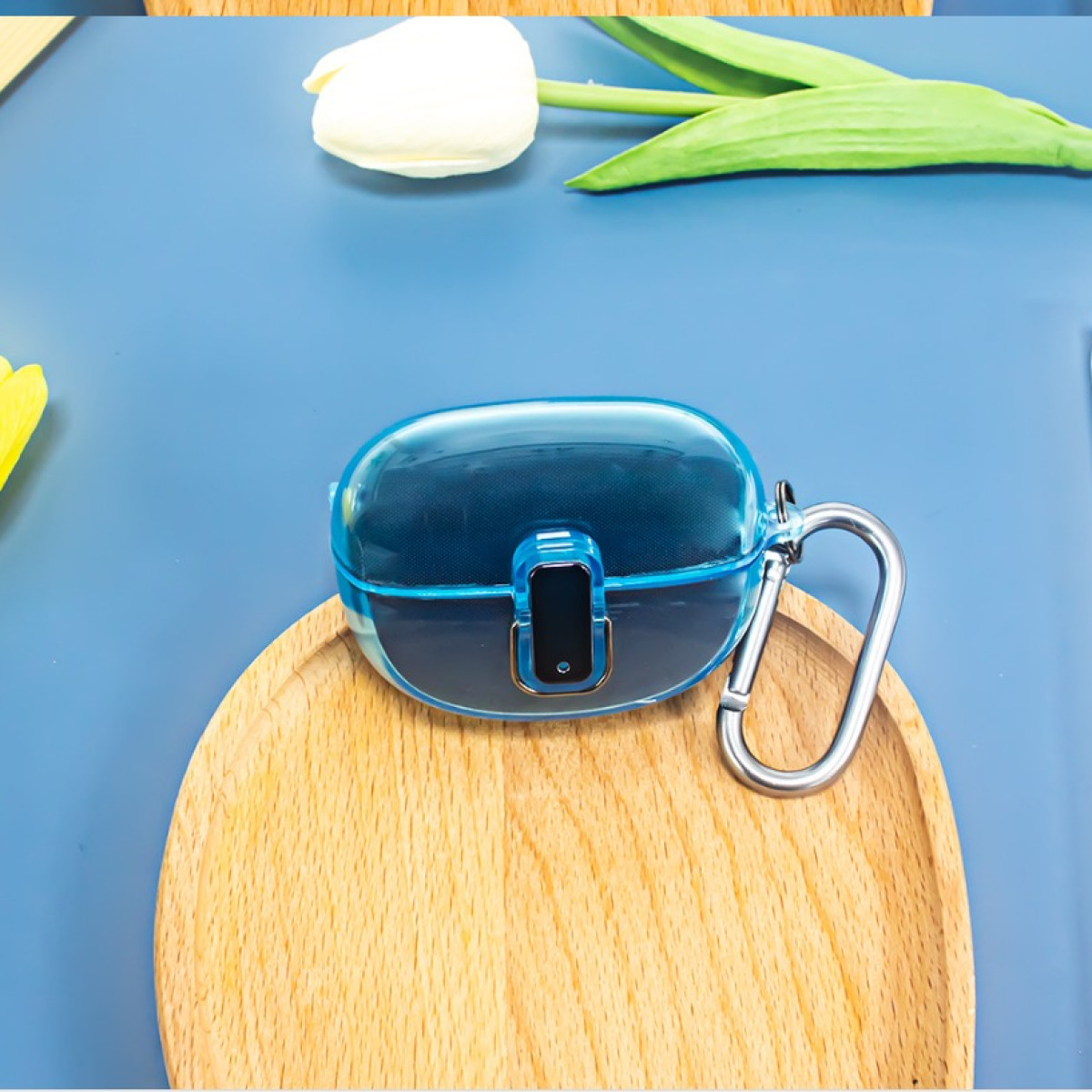Blaue Ohrhörerhülle mit silbernem Clip auf Holztablett mit weißer Tulpe auf blauer Oberfläche.