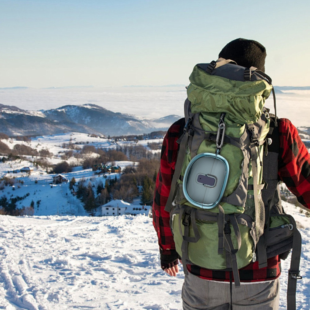Eine Person in Winterausrüstung mit Rucksack und blauem Ohrhöreretui, verschneiter Hintergrund.