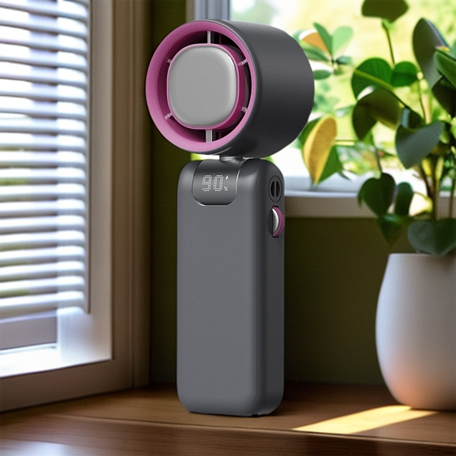 Ein schwarz-grauer Ventilator mit rosa Rand, steht auf einer Holzoberfläche, neben einer weißen Vase und Pflanze.