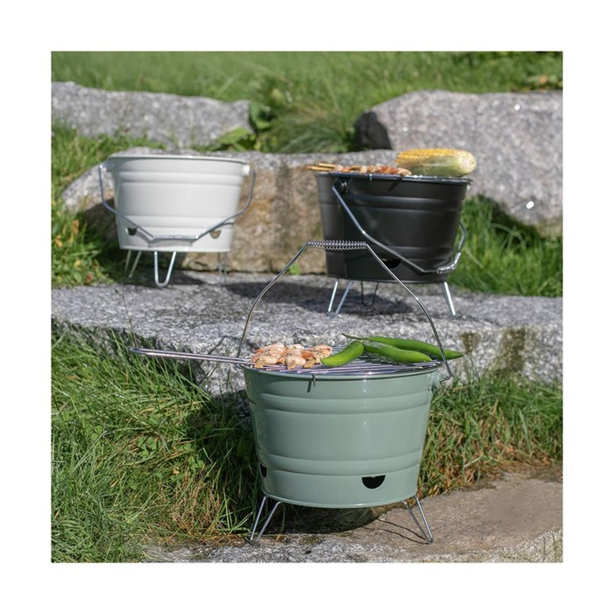 Three small grills. One white, one black, and one green, sit on rocks with grass.