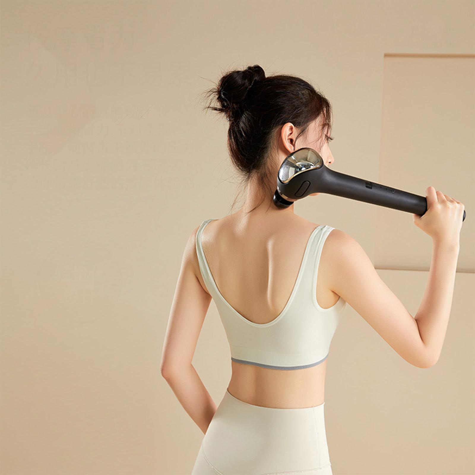 Eine Frau benutzt ein Massagegerät an ihrem oberen Rücken. Sie trägt einen Sport-BH und Leggings.