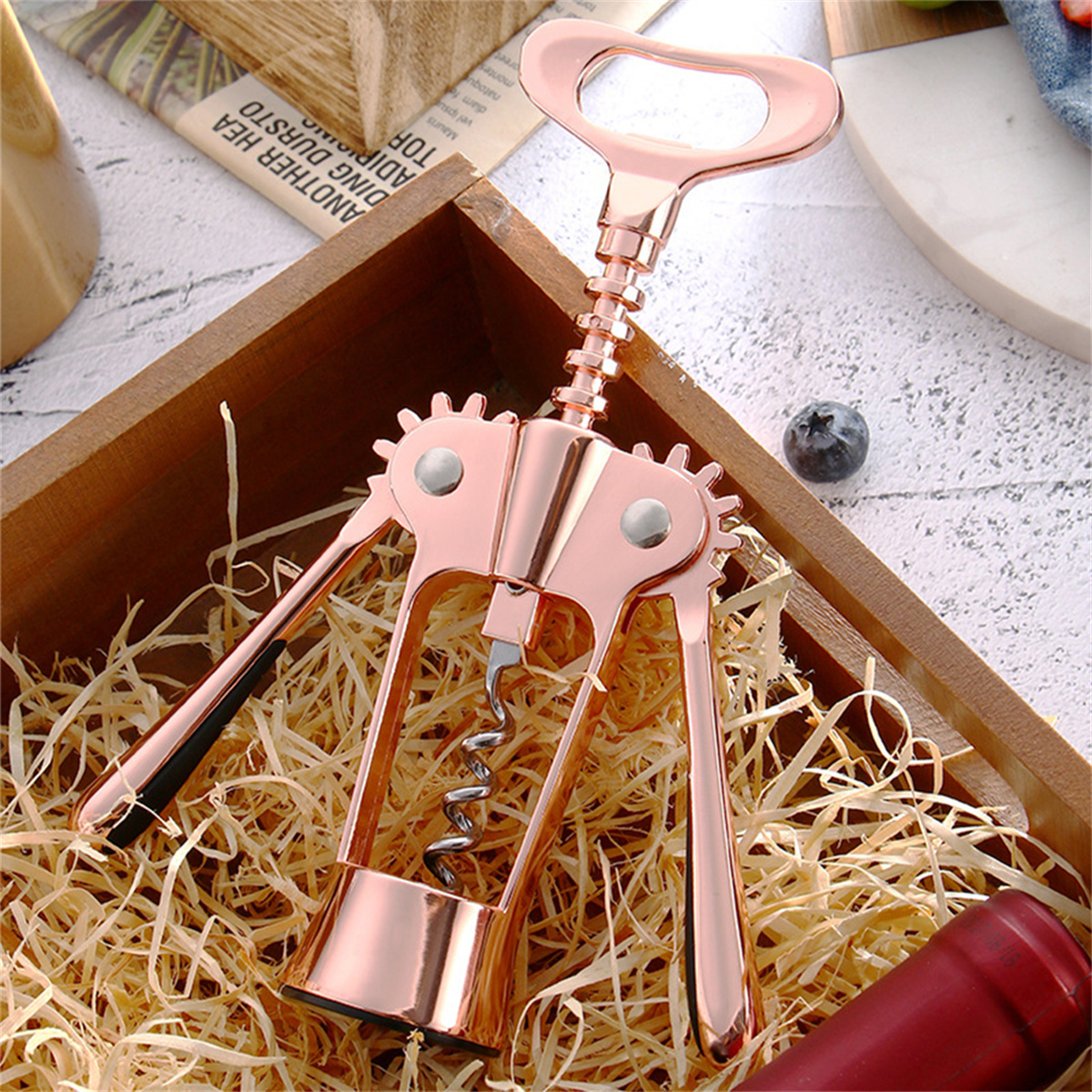 Ein roségoldener Weinöffner in einer Holzkiste mit Stroh, einem Korken und einer Blaubeere.