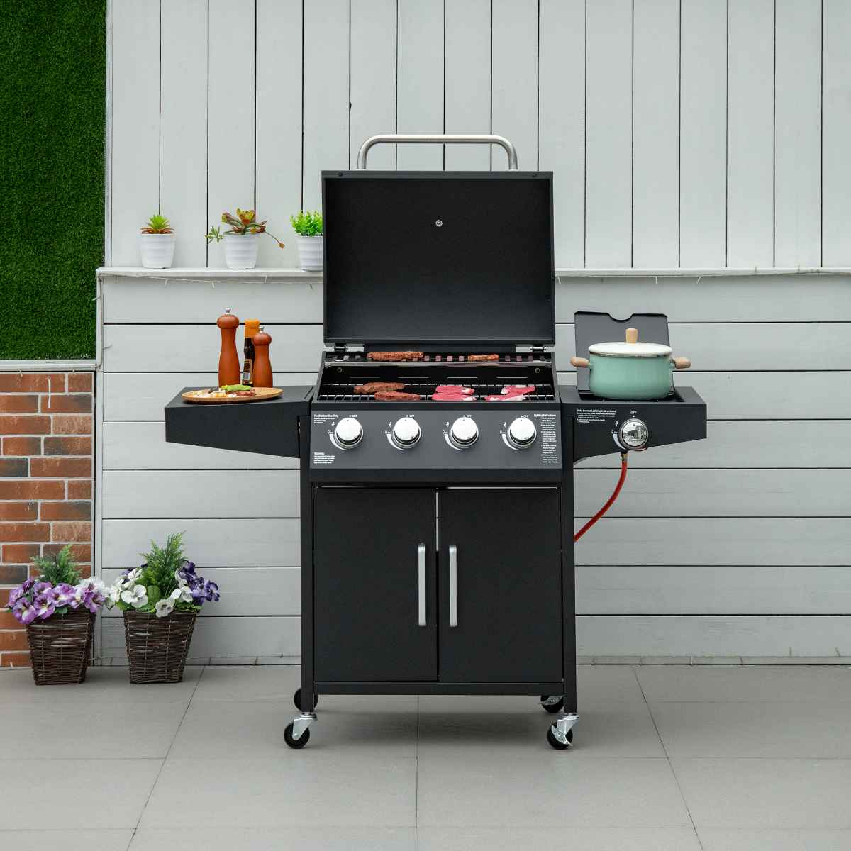 Schwarzer Gasgrill mit offenem Deckel auf einer Terrasse. Enthält Töpfe, Essen und Pflanzen.