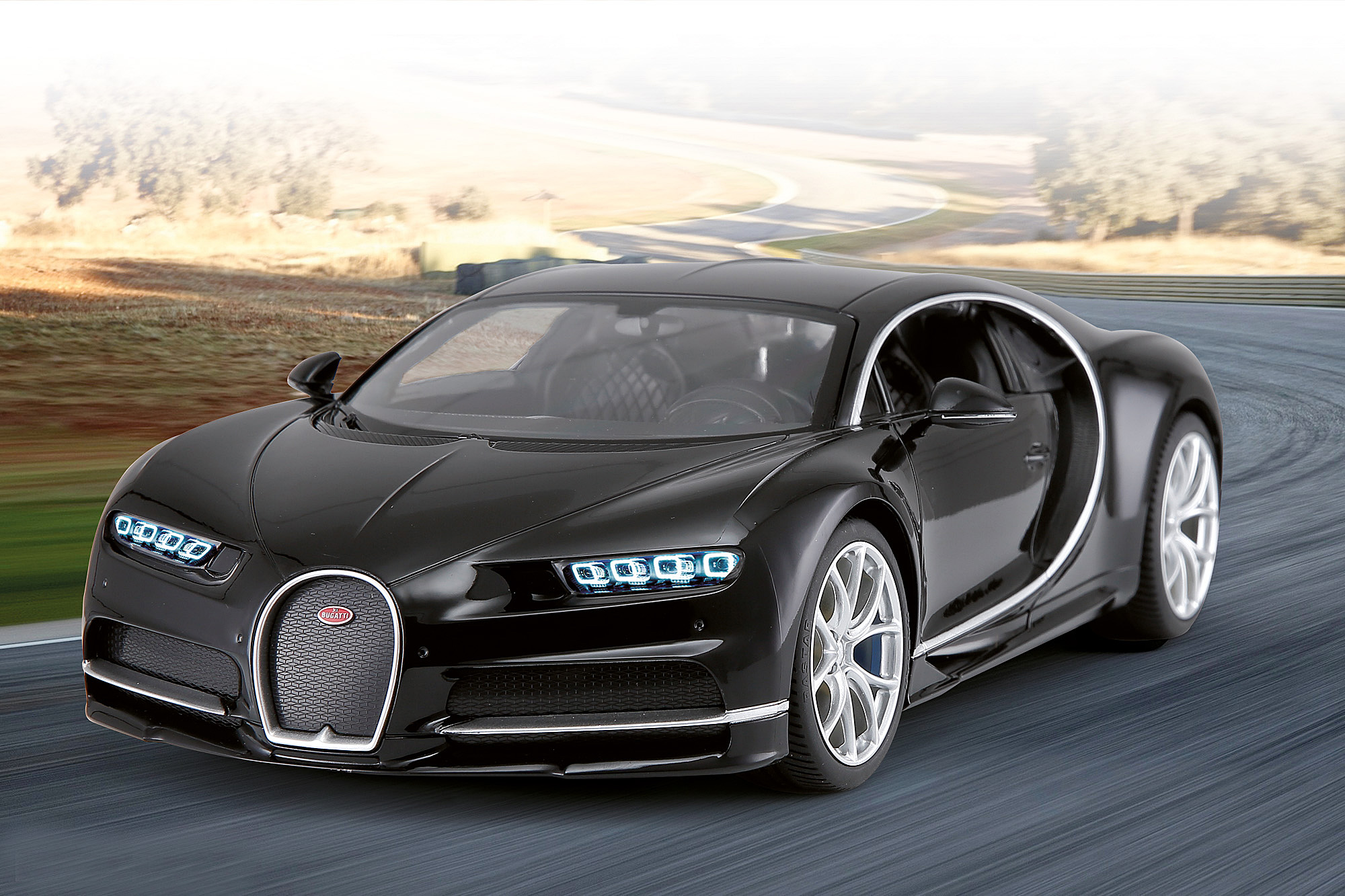 Schwarzes Bugatti Chiron Modellauto auf einer Rennstrecke. Das Auto ist in Bewegung, die Scheinwerfer sind an.