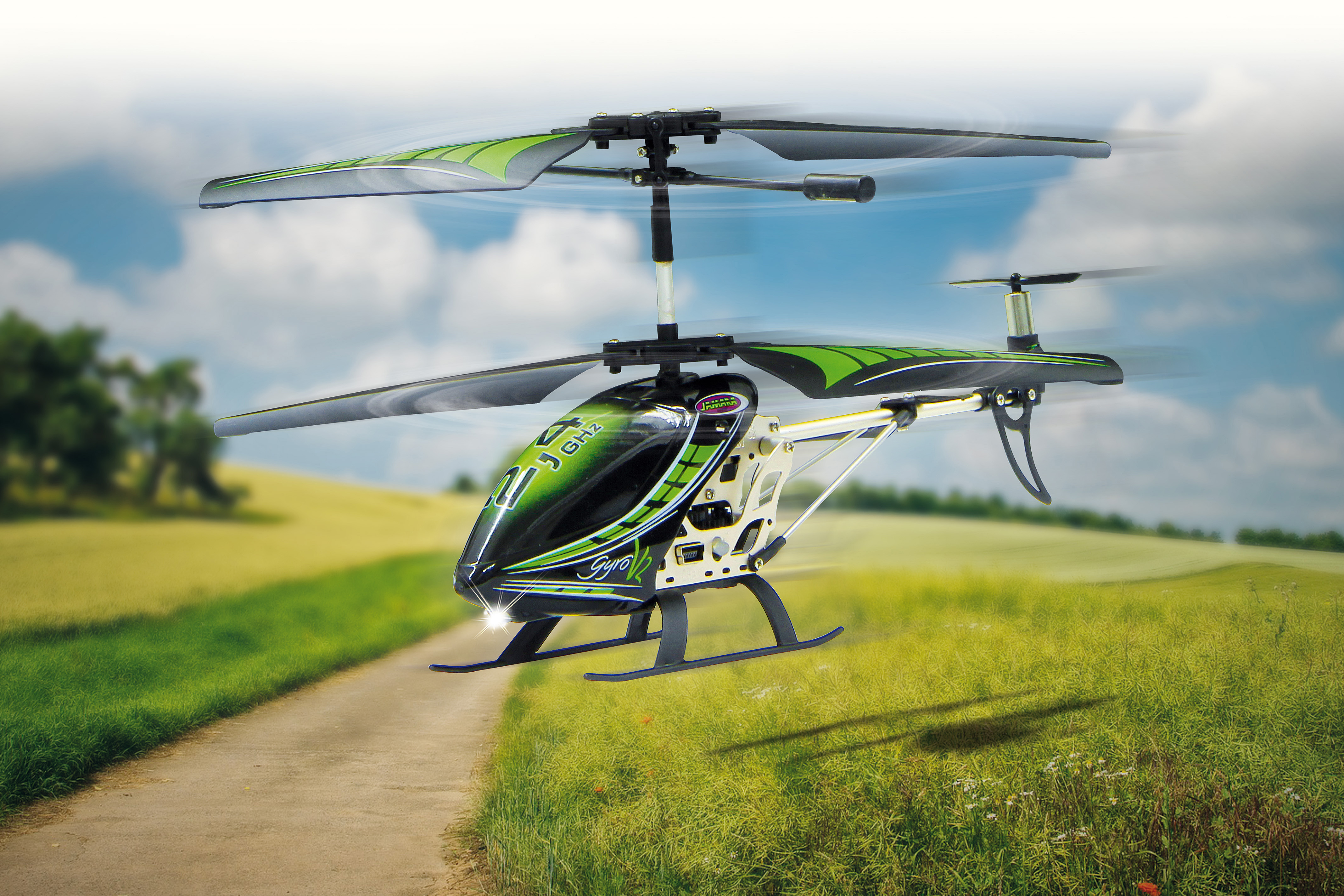Schwarz-grüner Helikopter fliegt über einem Weg auf einem Feld. Blauer Himmel im Hintergrund.
