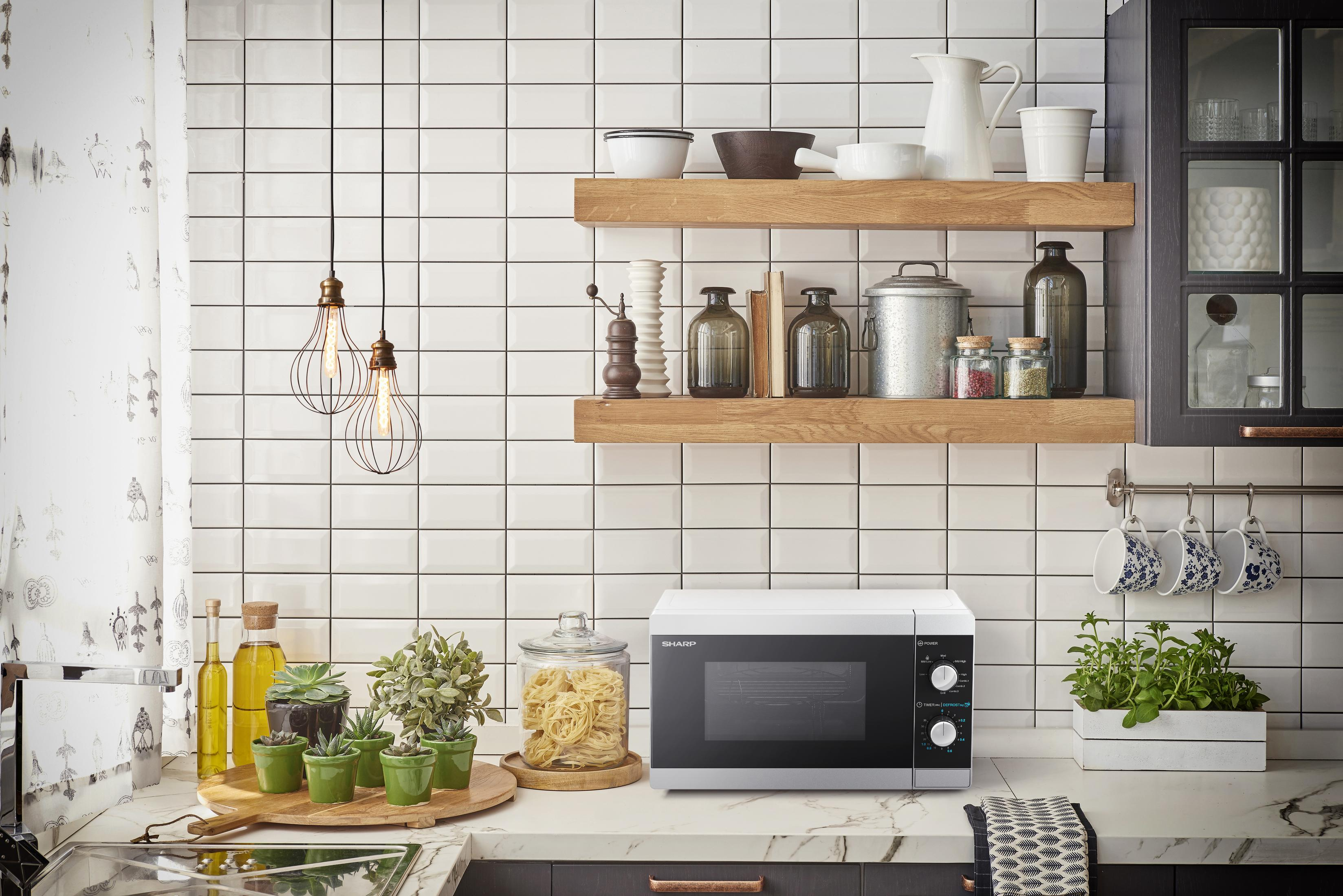 Scena kuchenna z kuchenką mikrofalową na blacie. Półki z przedmiotami powyżej. Rośliny i dekoracje.