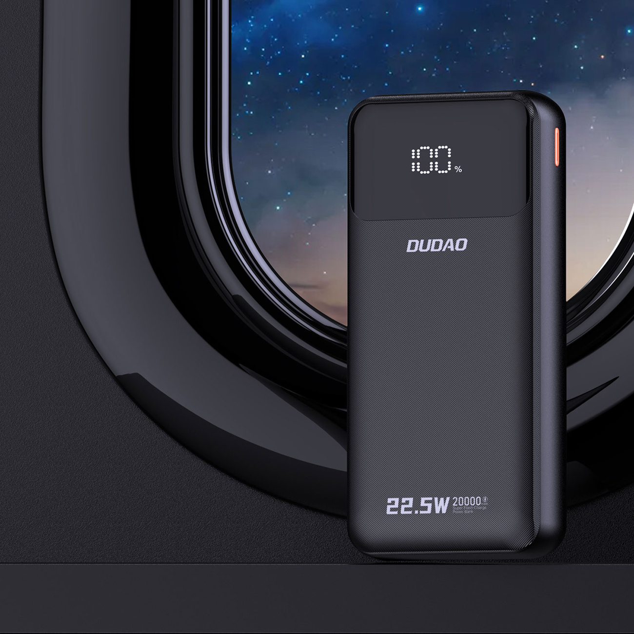 Eine schwarze Powerbank mit einem Bildschirm, der 100 % anzeigt. Es befindet sich in der Nähe eines Fensters mit Sternennachtblick.