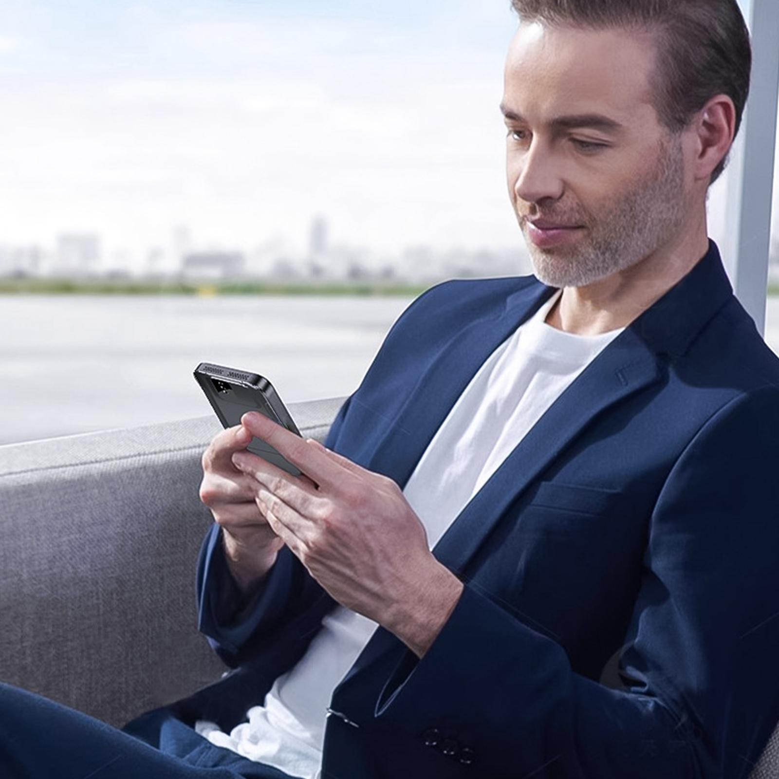 Ein Mann im Anzug sitzt und benutzt ein schwarzes Telefon. Es gibt einen verschwommenen Hintergrund.
