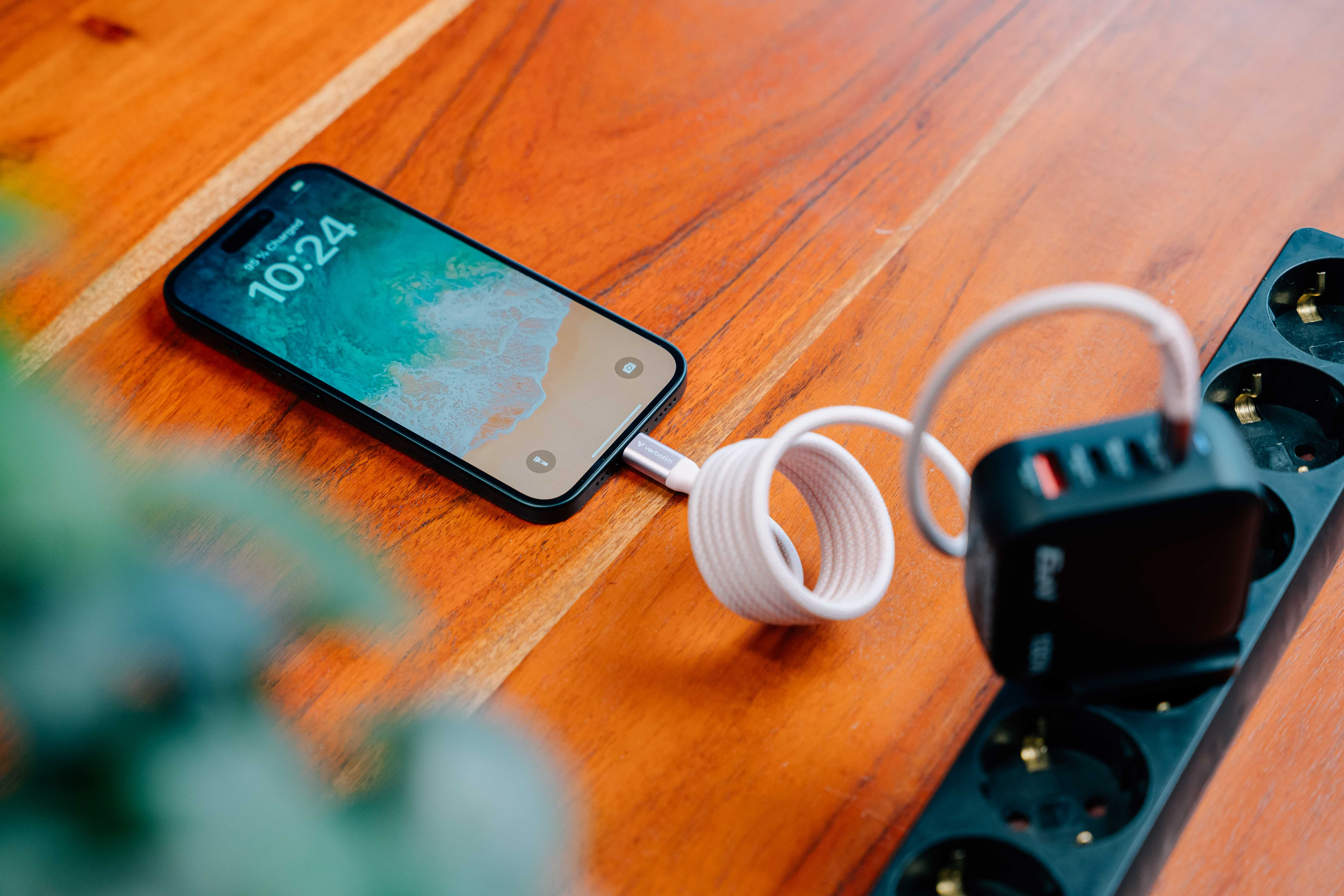 Een telefoon die oplaadt op een houten tafel. Een iPhone is verbonden met een oplader met een witte kabel. De tijd is 10:24.