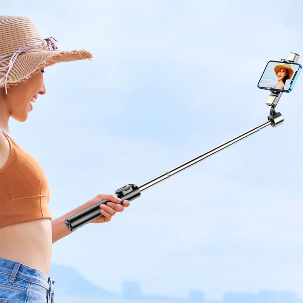 Frau benutzt einen Selfie-Stick. Sie trägt einen Hut und ein braunes Oberteil. Der Hintergrund ist blauer Himmel.