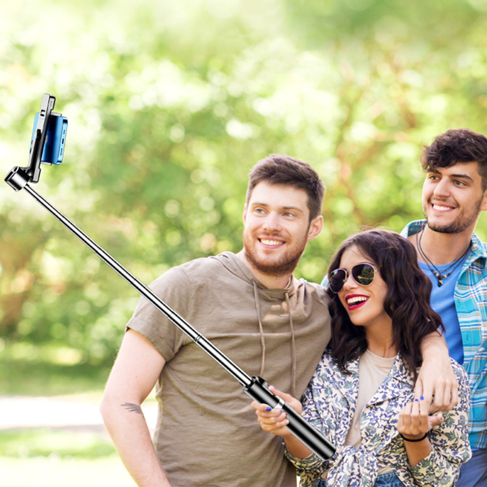 Drei lächelnde Personen machen ein Selfie mit einem Stick. Gr üne Bäume sind im Hintergrund.