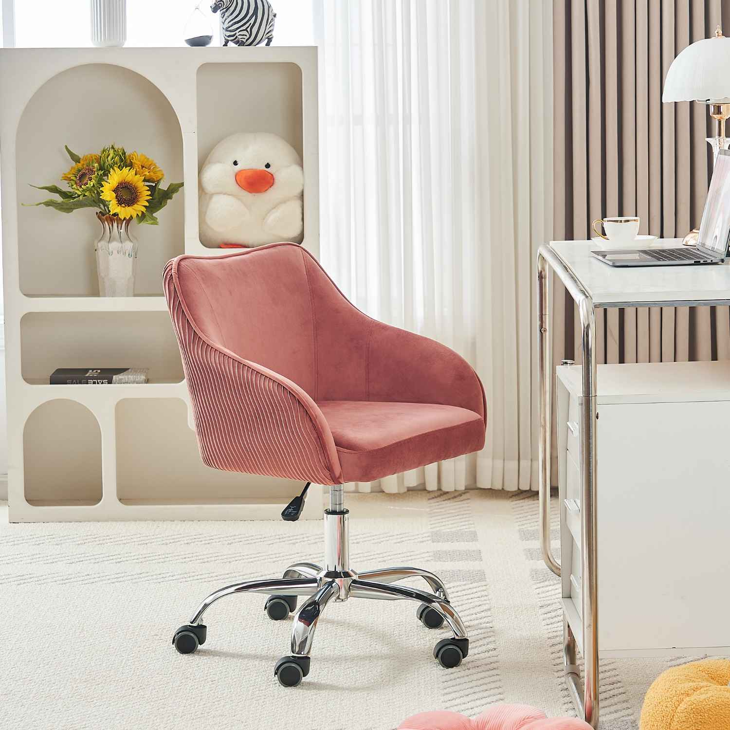 Ein rosa Samt-Bürostuhl in einem Raum. Der Stuhl steht vor einem weißen Schreibtisch und Regal.