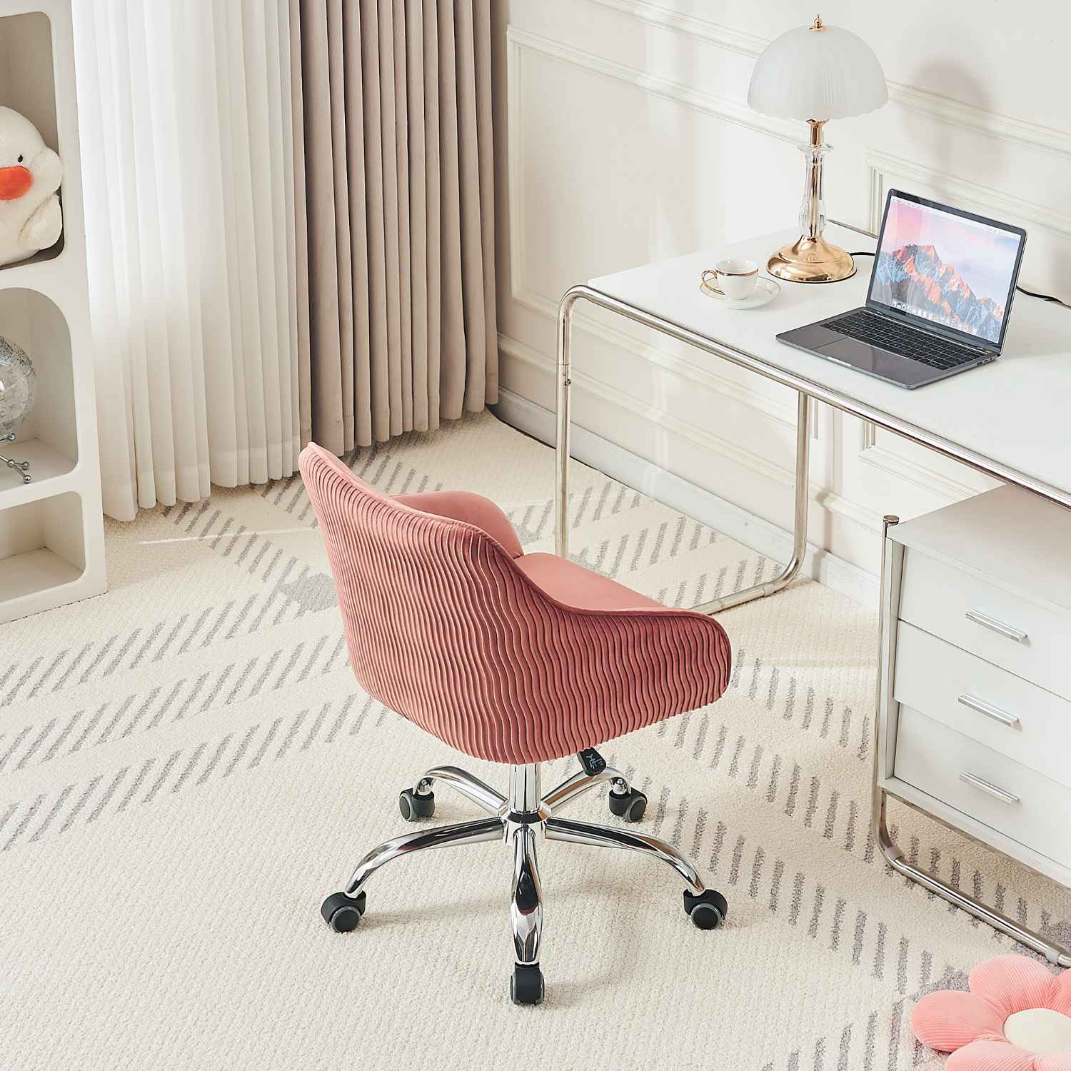 Ein rosa Bürostuhl steht vor einem Schreibtisch. Ein weißes Regal mit Dekorationen befindet sich links hinter dem Stuhl.
