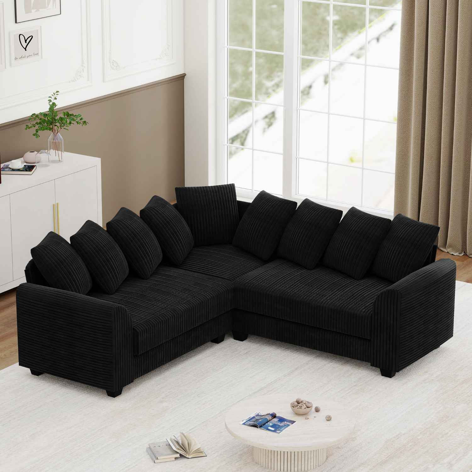 Schwarzes Cord-Ecksofa in hellem Raum mit weißen Wänden und Fenster.