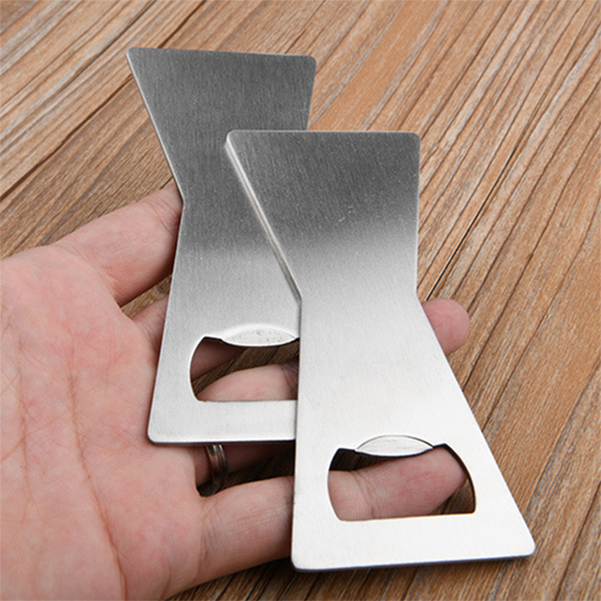 Zwei Metall-Flaschenöffner in der Hand. Sie sind silberfarben, mit einem einzigartigen geometrischen Design und einem Flaschenöffnungs-Schlitz.