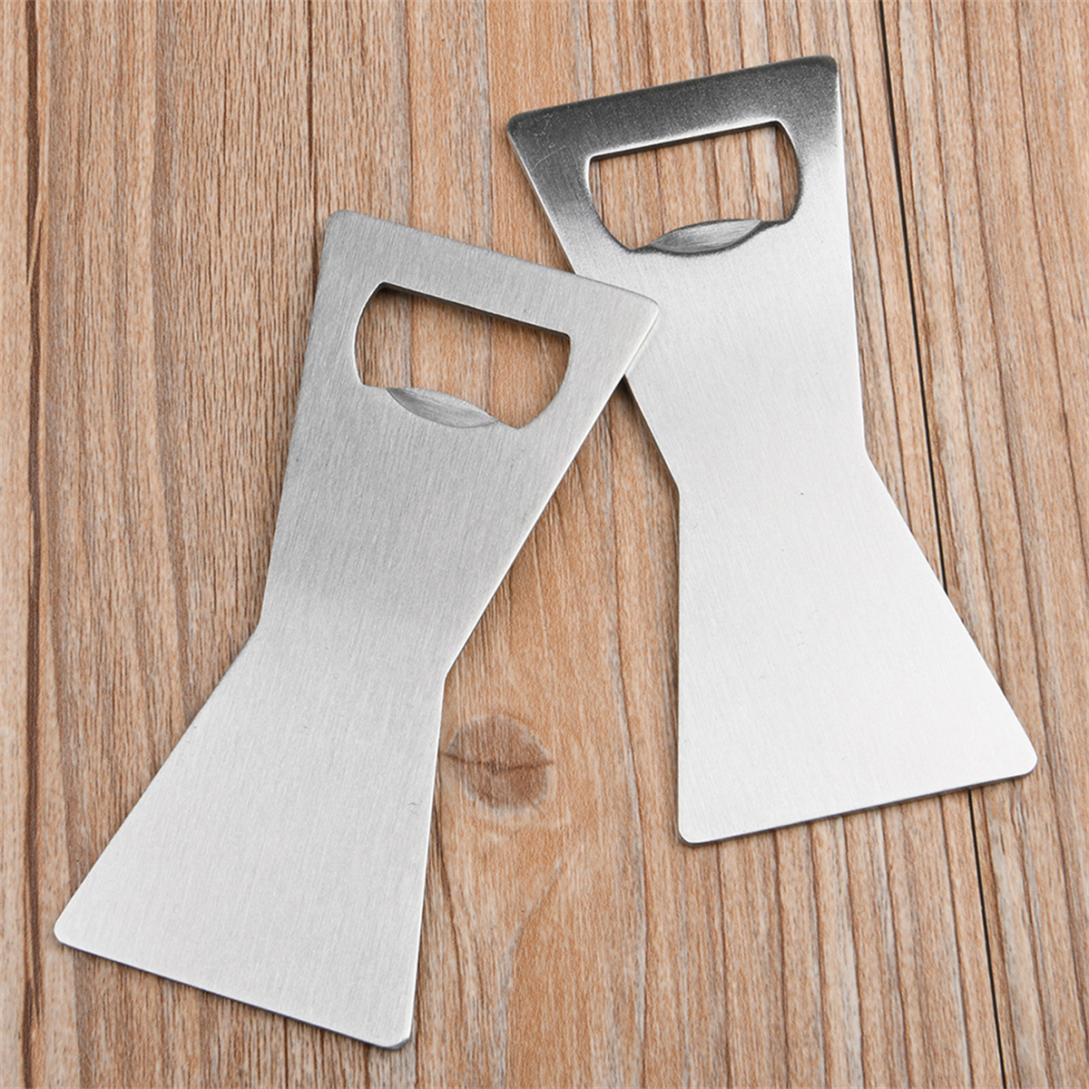 Zwei Metall-Flaschenöffner auf Holz. Sie sind silberfarben, mit einem einzigartigen geometrischen Design und einem Flaschenöffnungs-Schlitz.