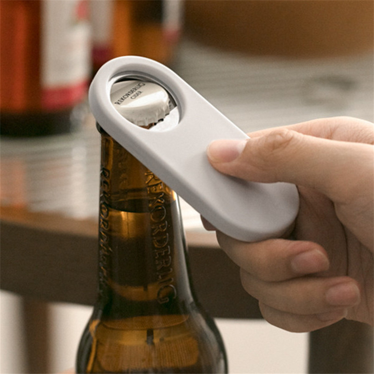 Eine Hand öffnet eine Bierflasche mit einem grauen Flaschenöffner. Die Flasche ist braun.
