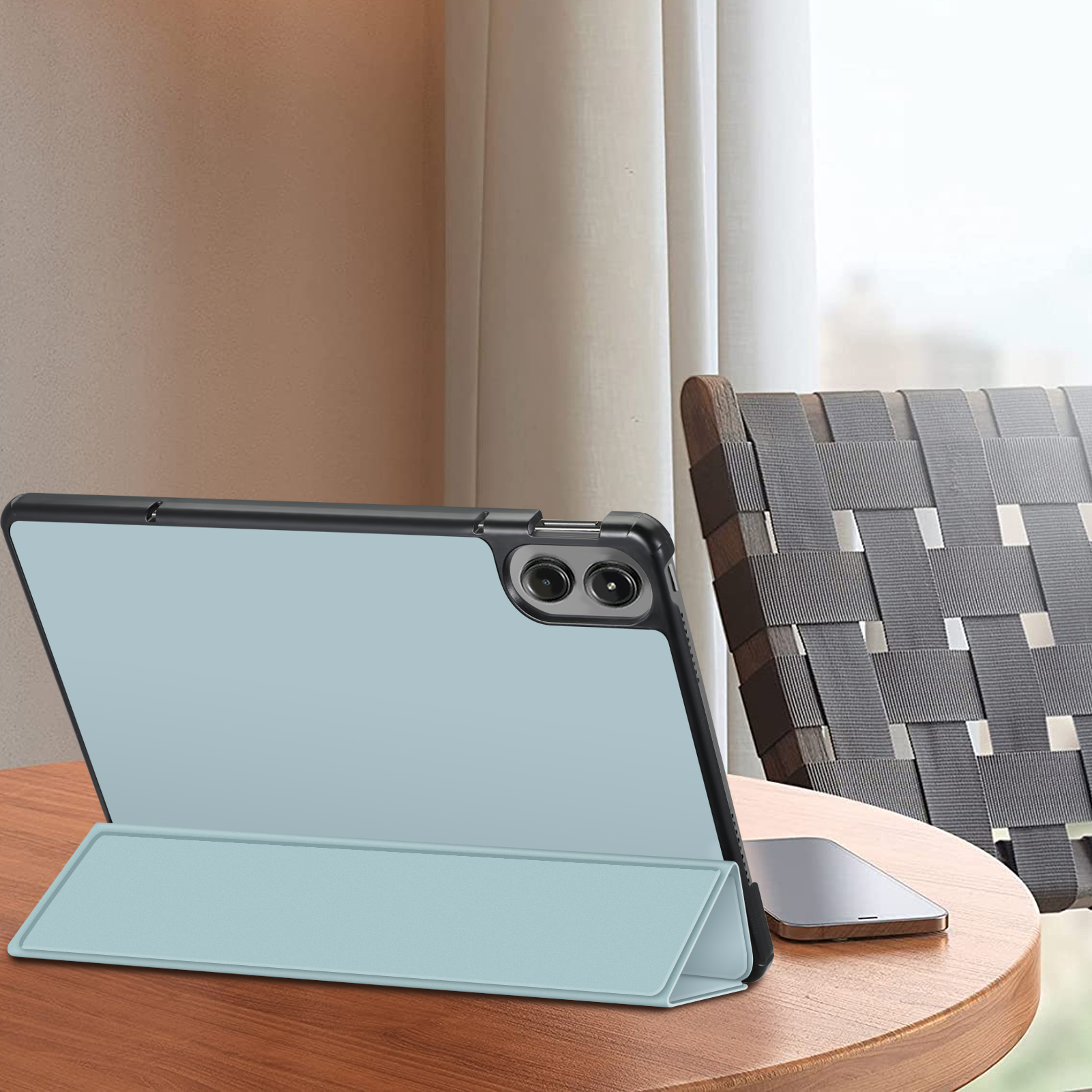 Ein Tablet mit hellblauer Hülle, offen, auf einem Tisch. Ein Telefon und ein Stuhl sind im Hintergrund.