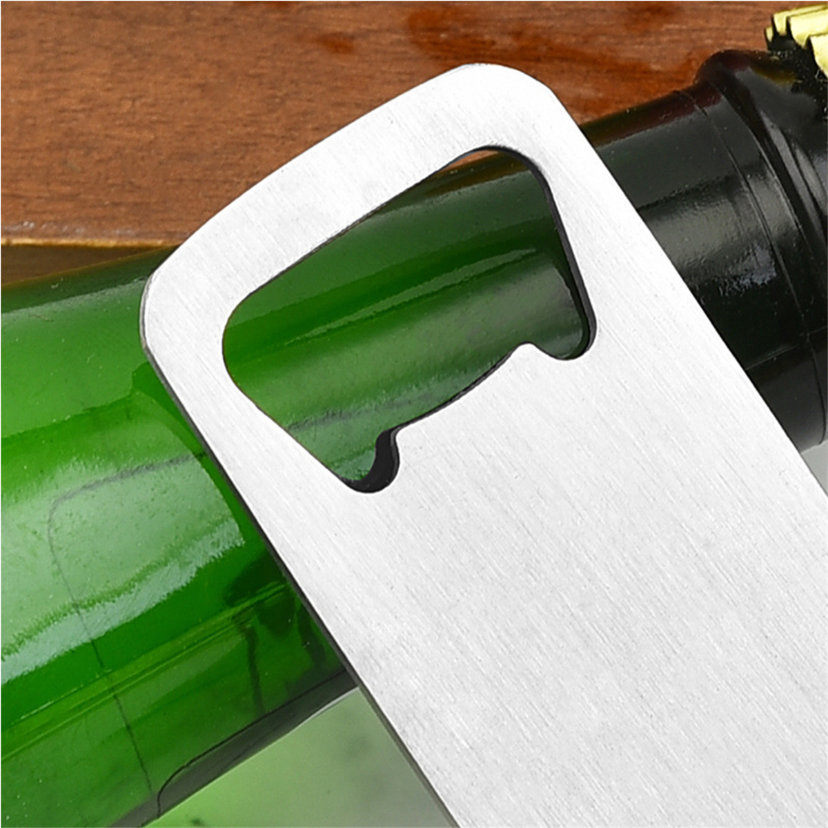 Nahaufnahme eines silbernen Flaschenöffners auf einer Holzoberfläche. Eine grüne Bierflasche ist im Hintergrund.