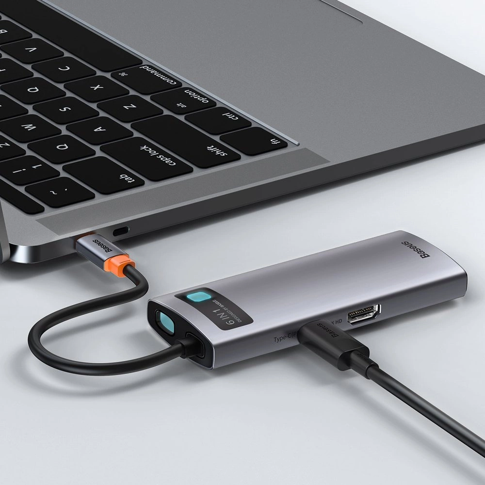 Laptop ze srebrnym hubem, z USB-C i innymi portami. Czarny kabel do laptopa.