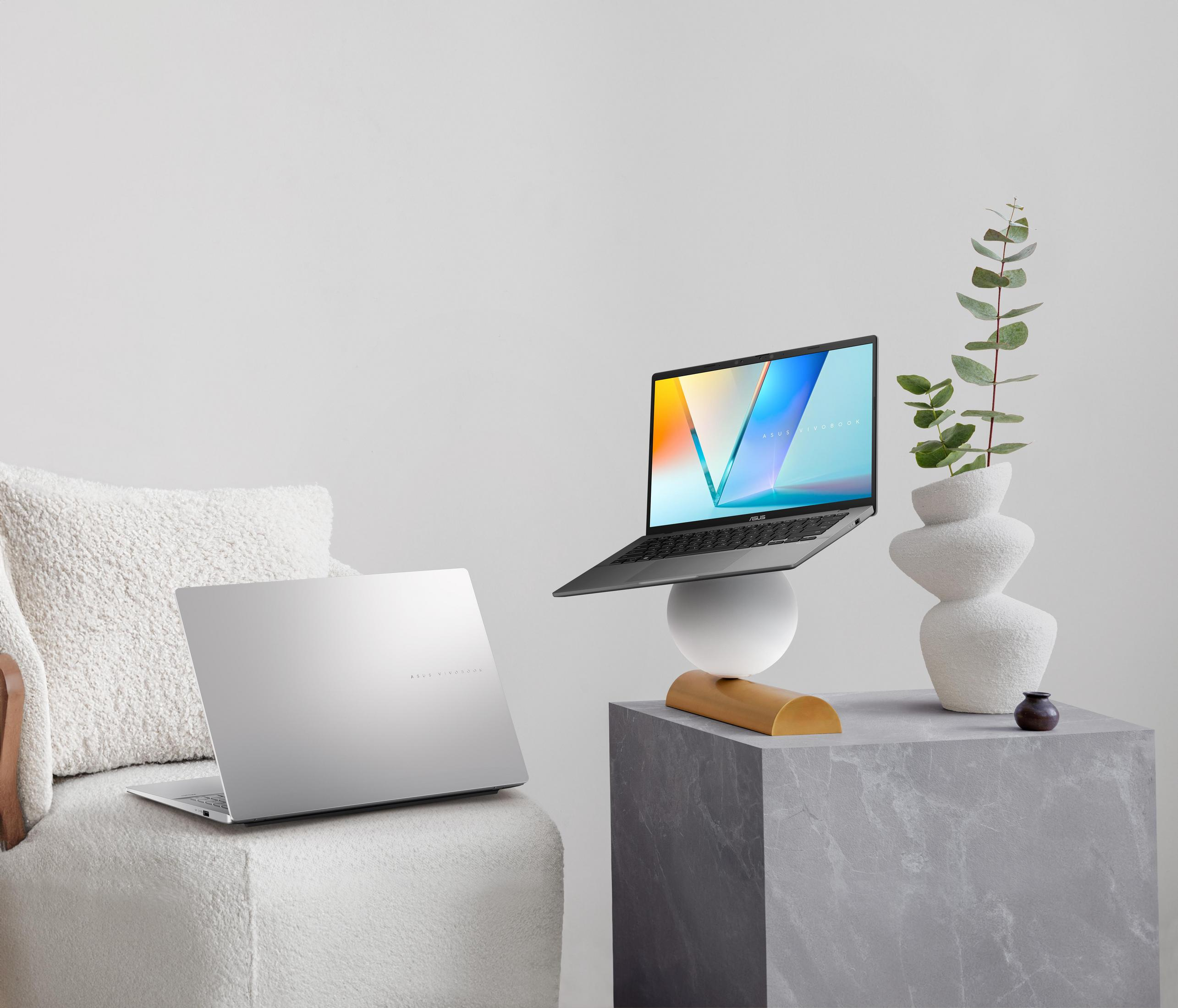 Laptop auf weißem Sockel, mit Deko. Weißes und graues Zimmer. Couch und Vase.