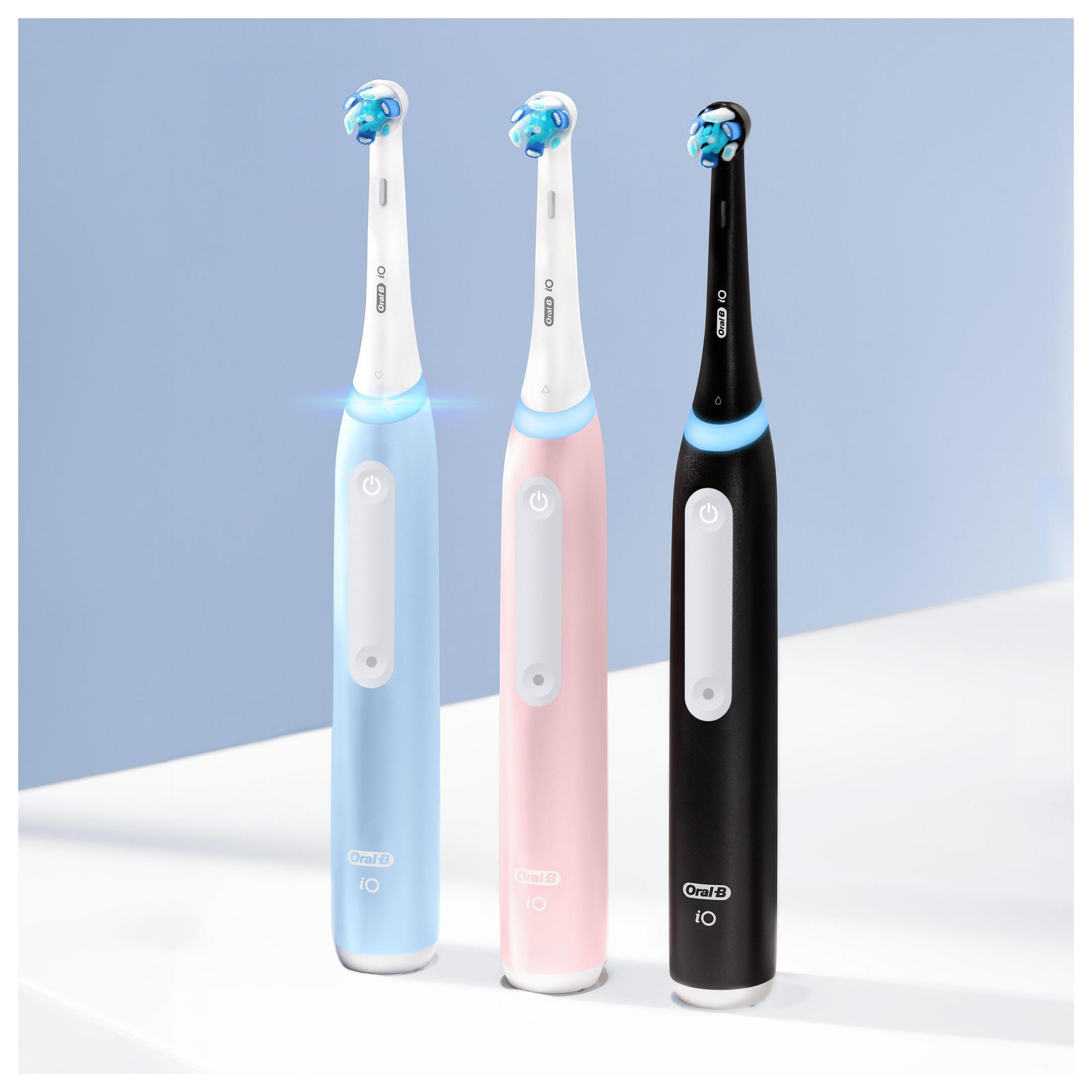 Drei elektrische Zahnbürsten in Pastellfarben, blau, rosa und schwarz, auf einer weißen Oberfläche.
