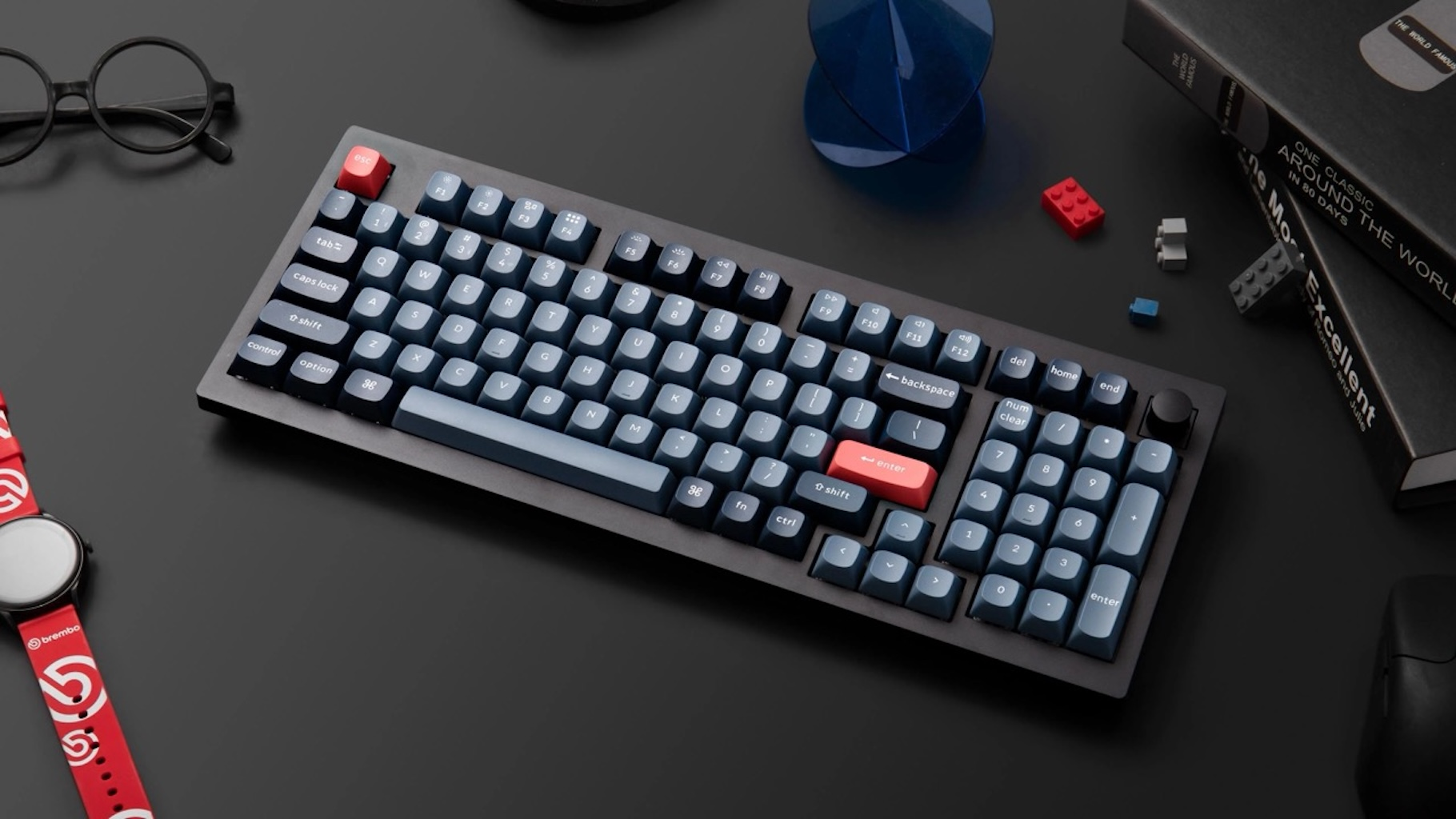Czarna klawiatura z niebieskimi klawiszami, czerwonymi klawiszami i różnymi przedmiotami na ciemnej powierzchni.