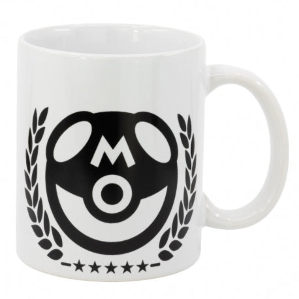 Una taza blanca con un logotipo de cara sonriente negra con la letra 'M' en el medio y rodeado de hojas.