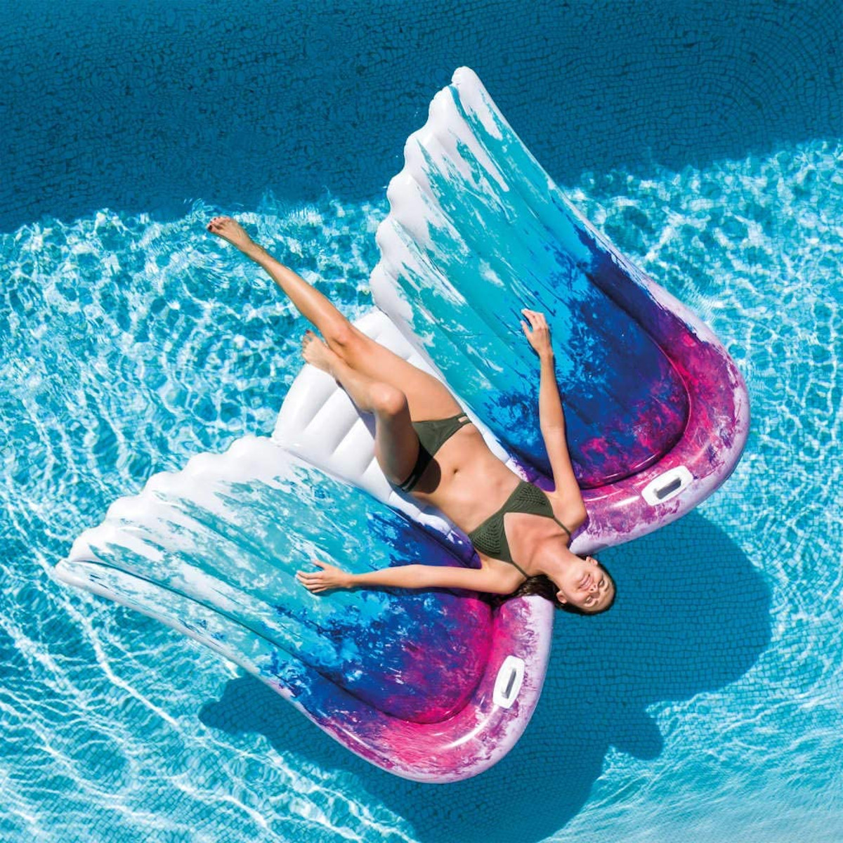 Eine Frau liegt auf einem bunten Pool-Float in Form von Engelsflügeln in einem Schwimmbad.