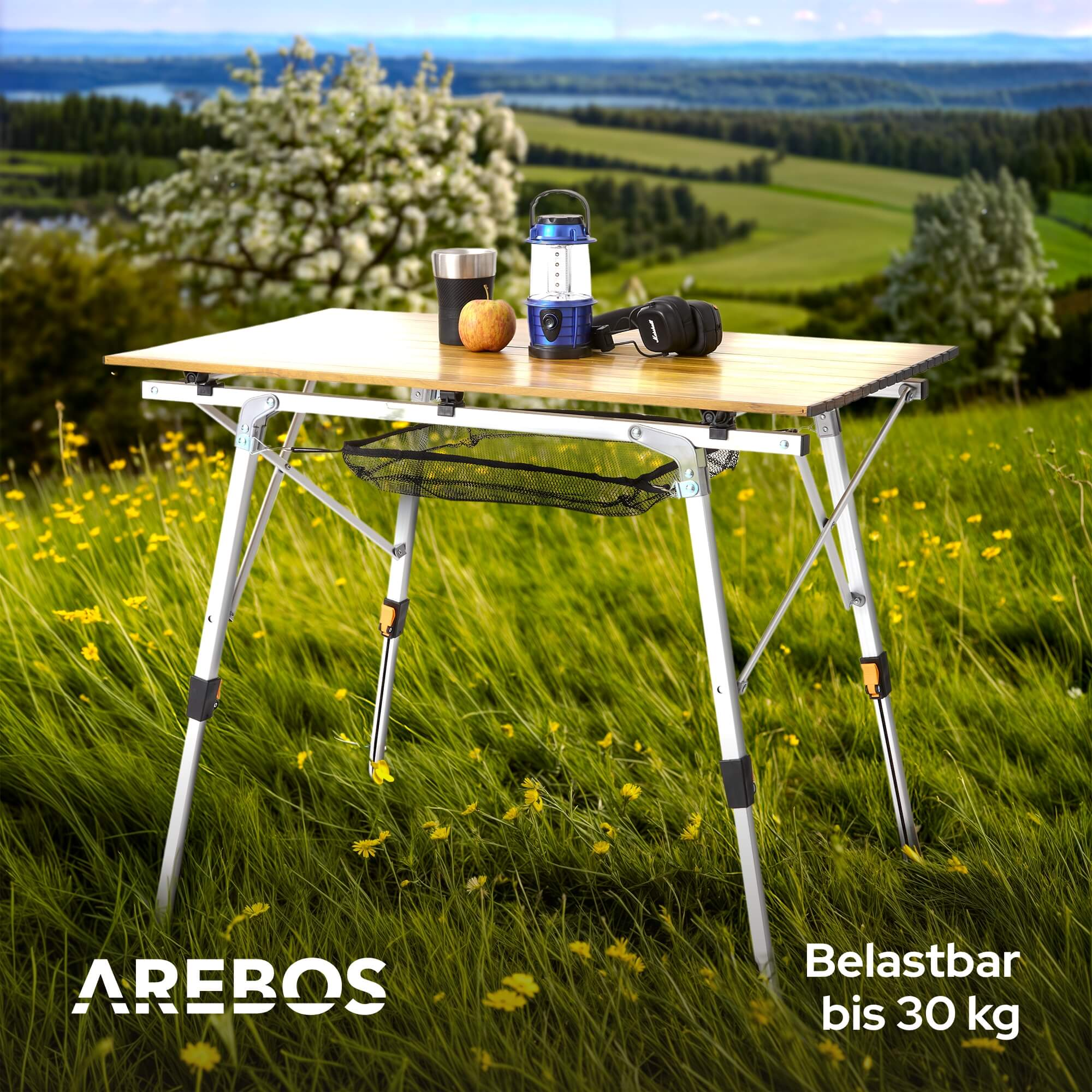 Ein Klapptisch auf Gras, mit Lampe, Becher, Apfel und Kopfhörern. Er hat ein Netz und das AREBOS-Logo.