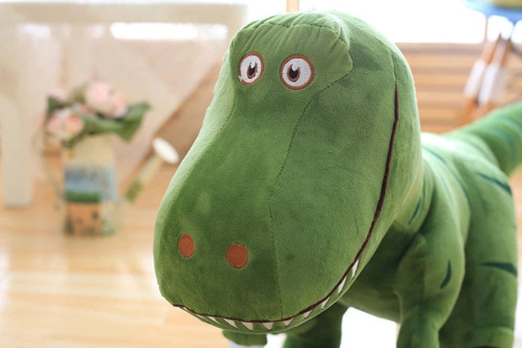 Ein grünes Dinosaurier-Plüschtier, Nahaufnahme des Gesichts, mit großen Augen und einem weißzahnigen Lächeln.