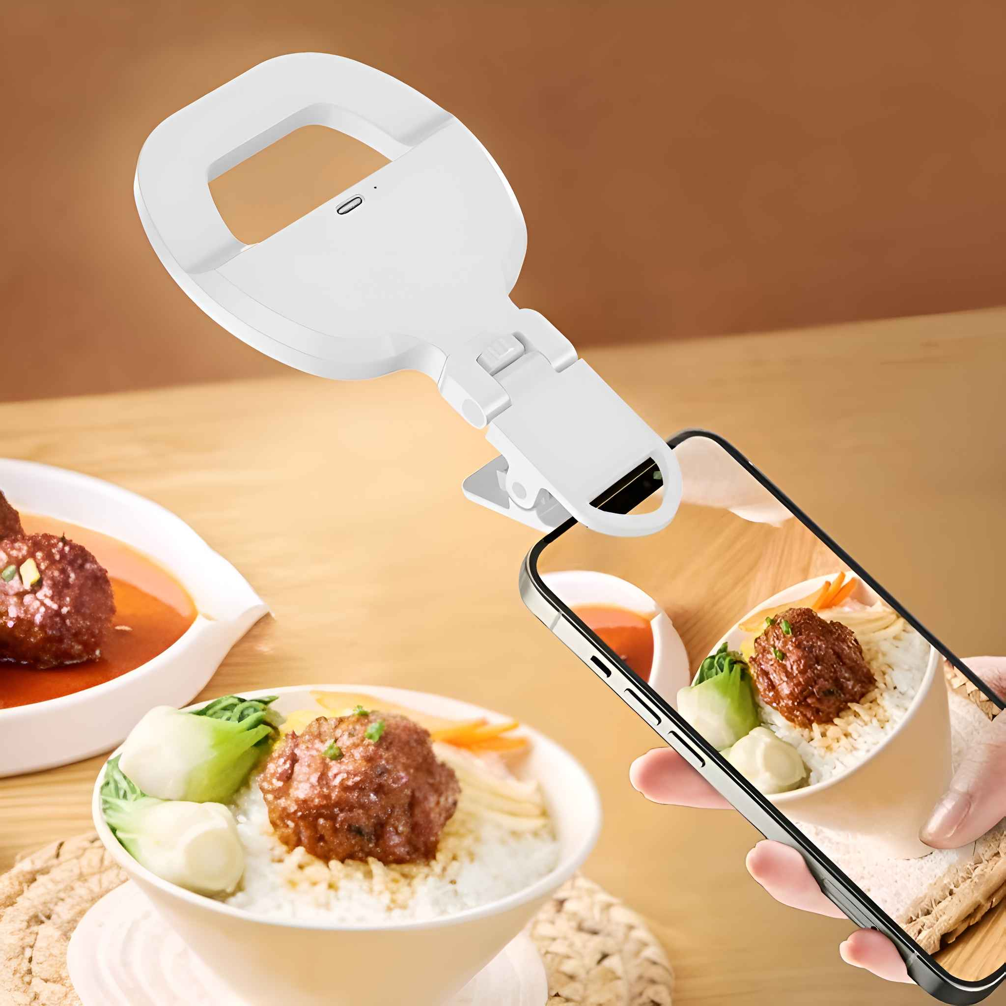 Ein Ringlicht ist an einem Telefon befestigt und macht ein Foto von einer Schüssel mit Essen mit Fleischbällchen und Gemüse. Der Hintergrund ist unscharf.