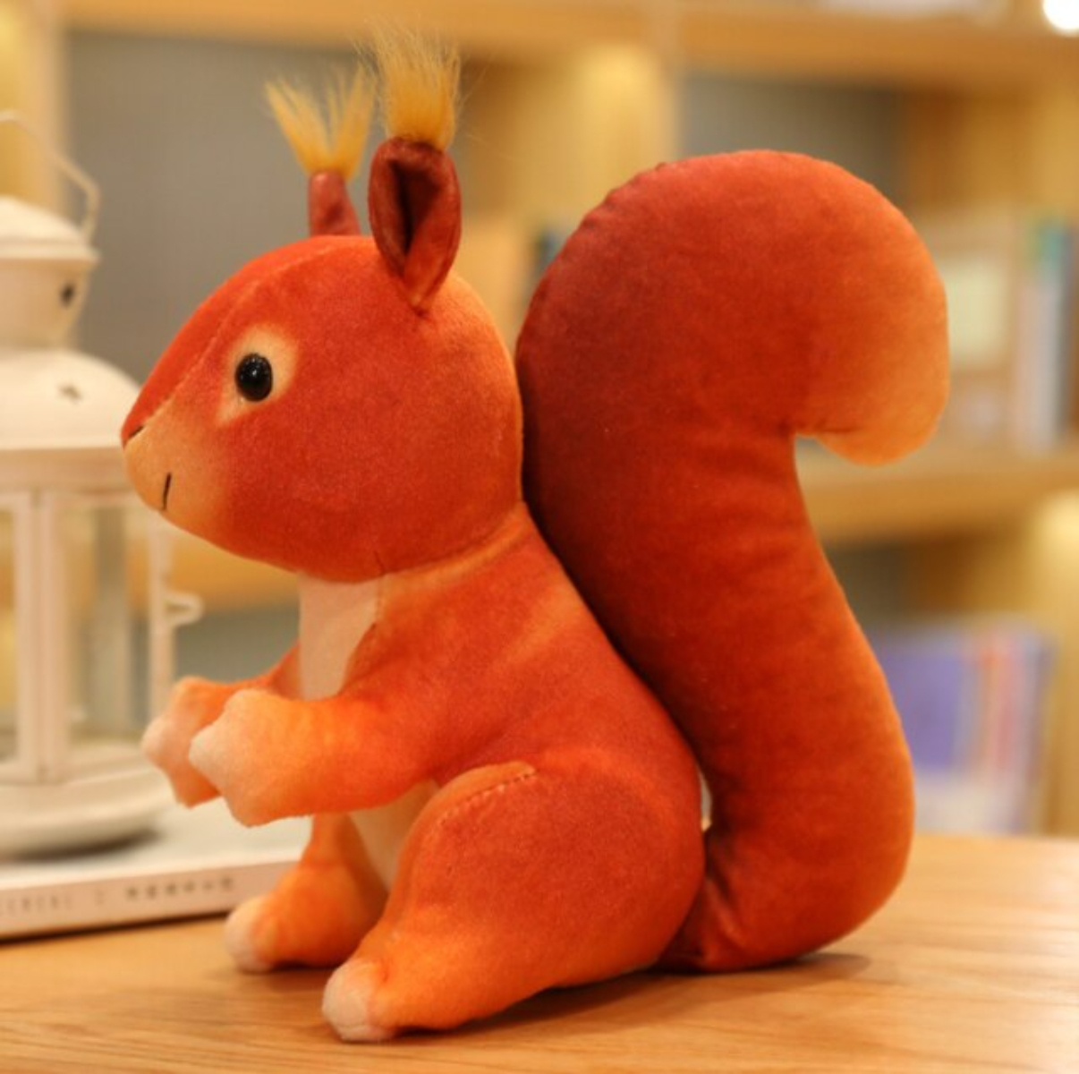 Ein orangefarbenes Stoff-Eichhörnchen sitzt. Es hat einen flauschigen Schwanz und sitzt auf Holz.