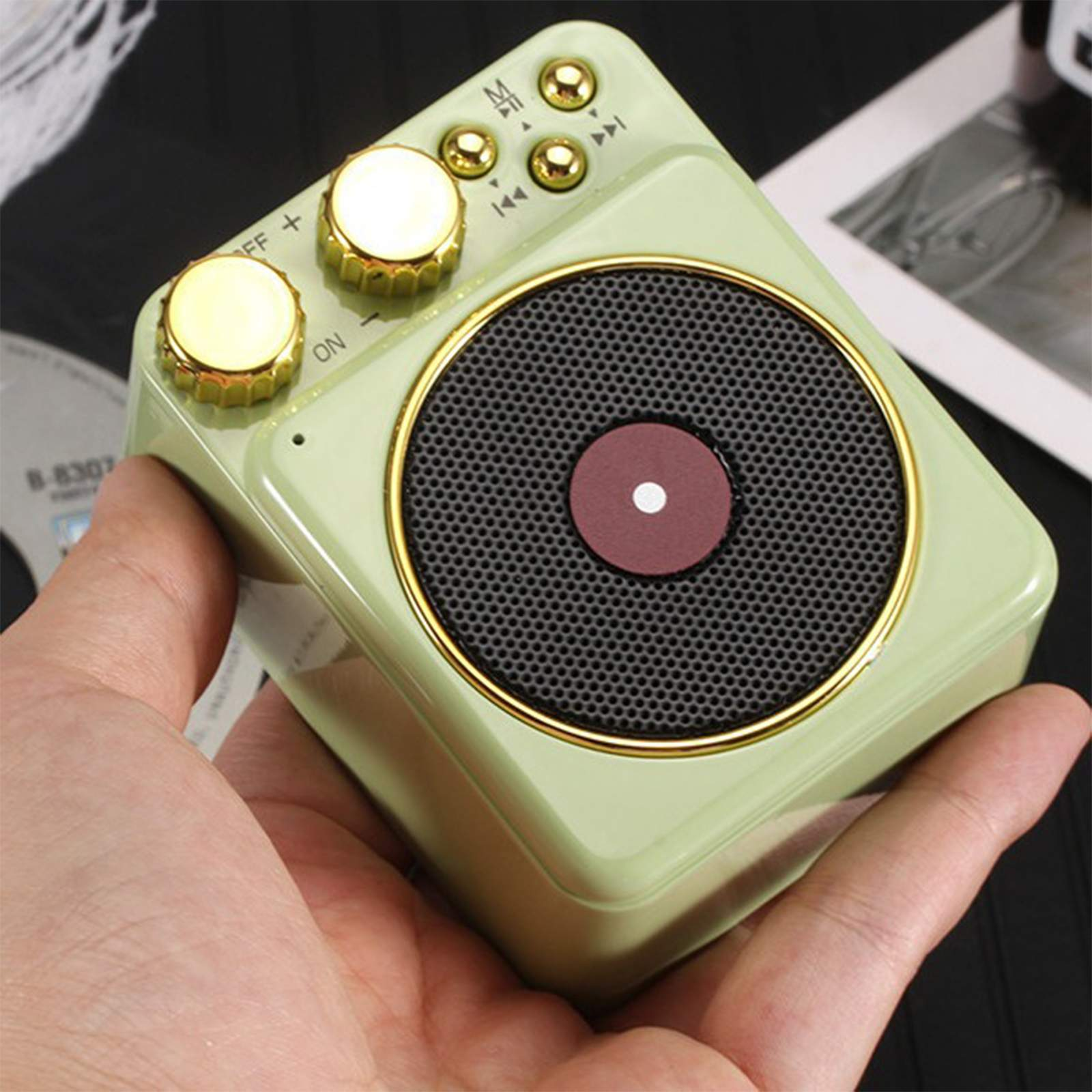 Grüner Retro-Lautsprecher mit goldenen Akzenten. Braune Lautsprecherabdeckung. Knöpfe oben. Hand hält den Lautsprecher.