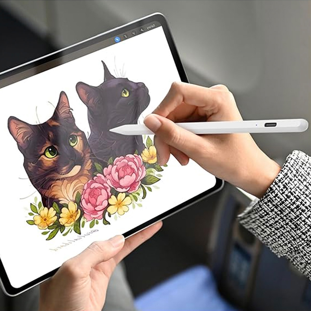 Eine Hand, die einen Stift verwendet, um Katzen auf einem Tablet zu zeichnen. Der Bildschirm zeigt zwei Katzen und Blumen.