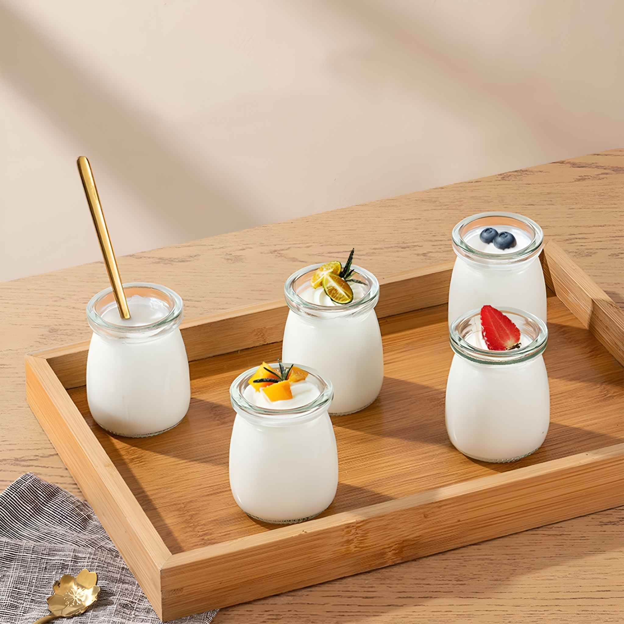 Ein Holztablett mit Joghurt in Gläsern, mit Fruchtbelägen. Ein goldener Löffel liegt im Tablett.