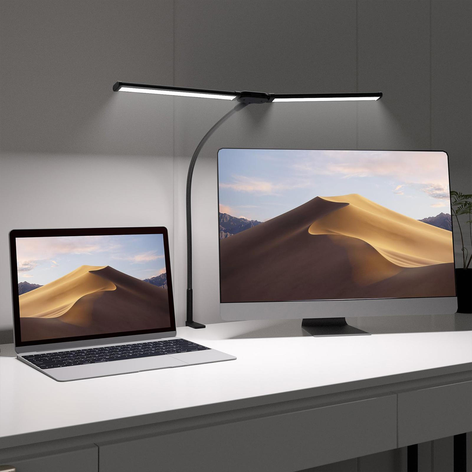 Eine schwarze Schreibtischlampe beleuchtet einen Schreibtisch mit Monitor und Laptop. Der Hintergrund zeigt Wüste.