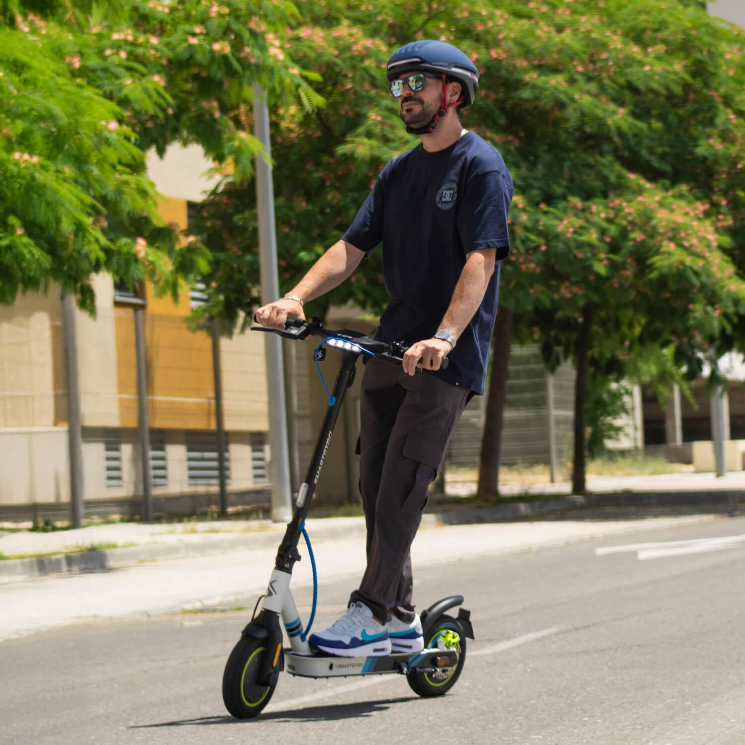 Hombre montando un scooter blanco y negro en una carretera. Lleva un casco.
