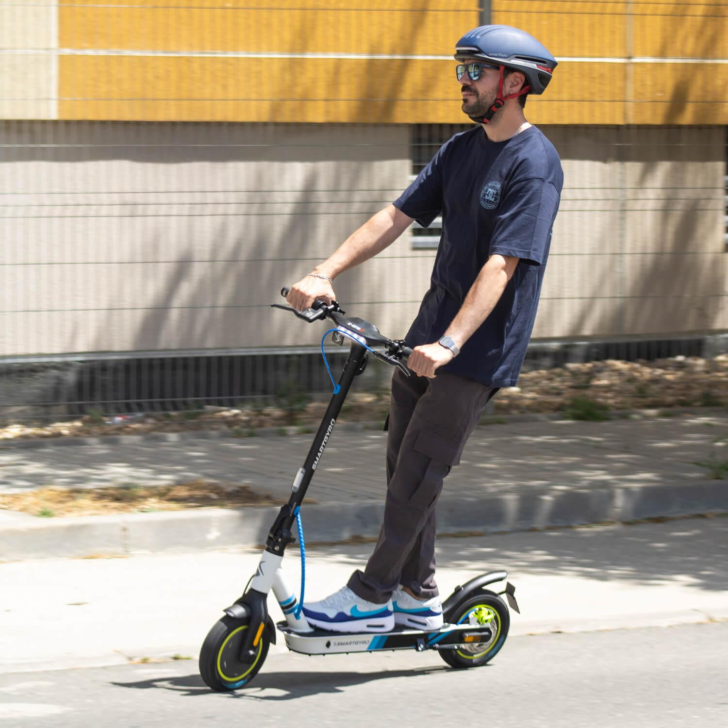 Hombre montando un scooter blanco y negro en una carretera. Lleva un casco.