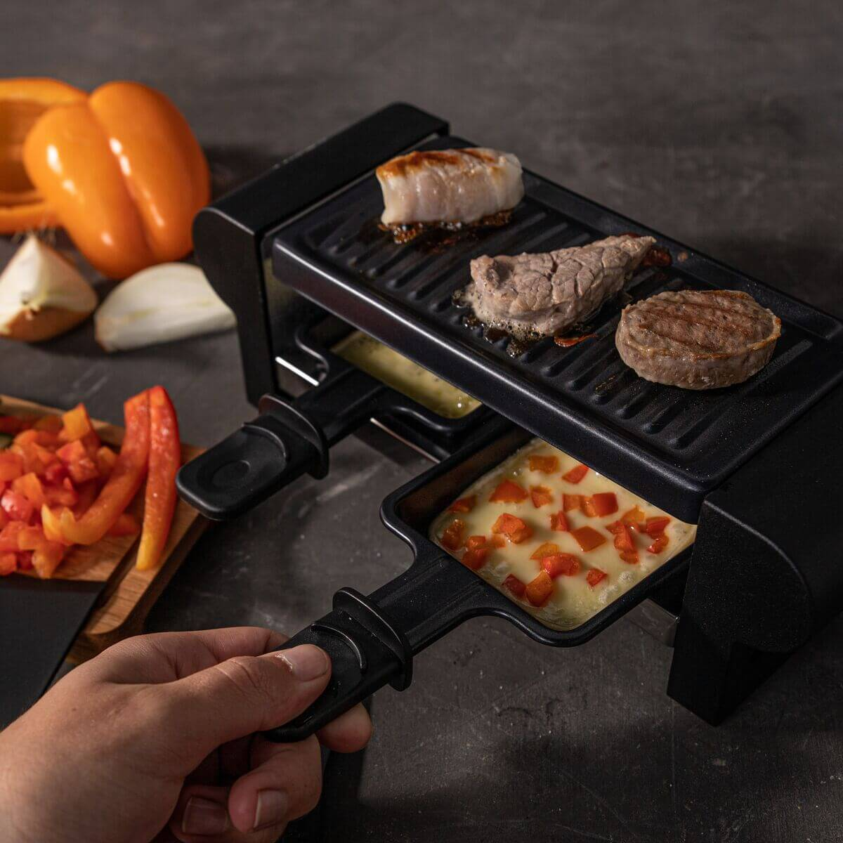 A person is grilling cheese and meat on a raclette grill.