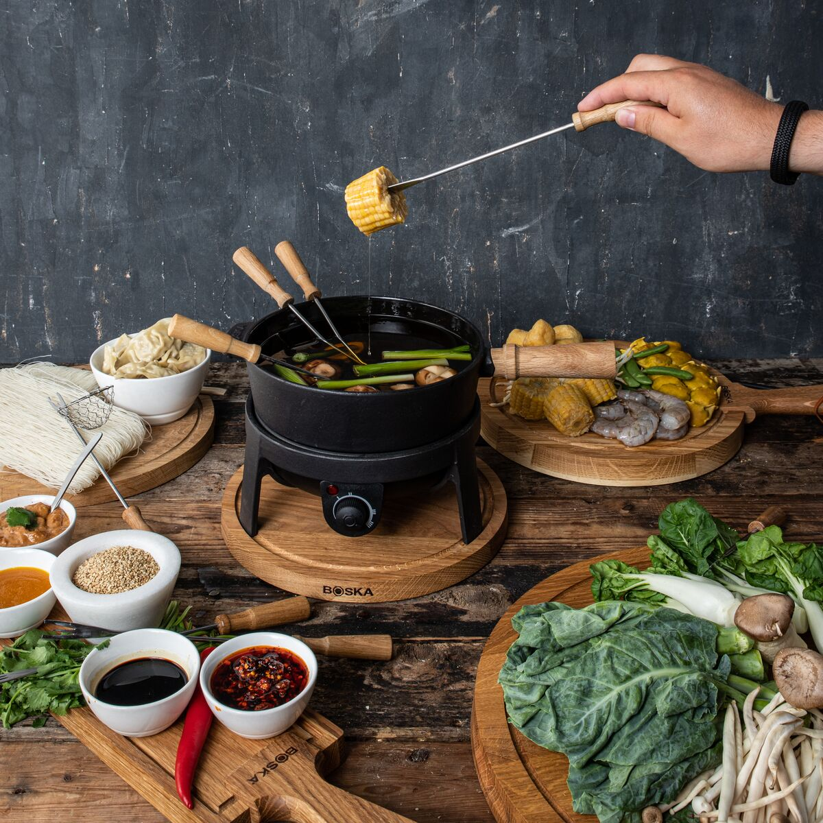 A fondue set with various food items on a wooden table.